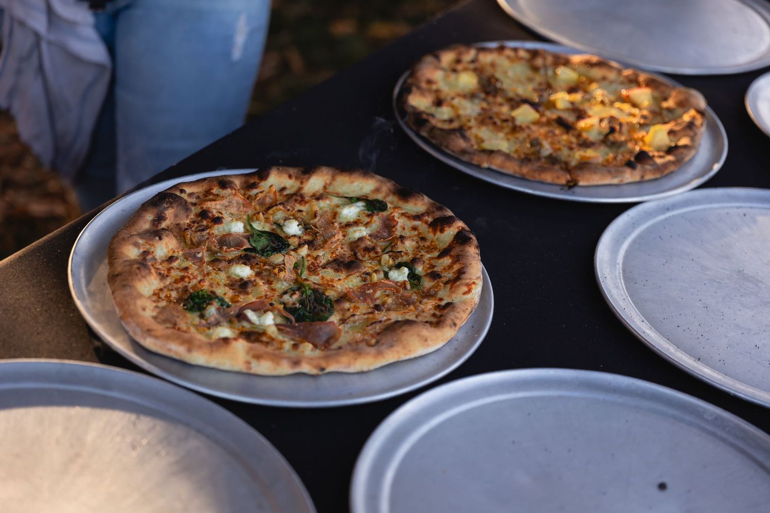 Freshly baked pizzas with various toppings arranged on white plates in a restaurant setting.