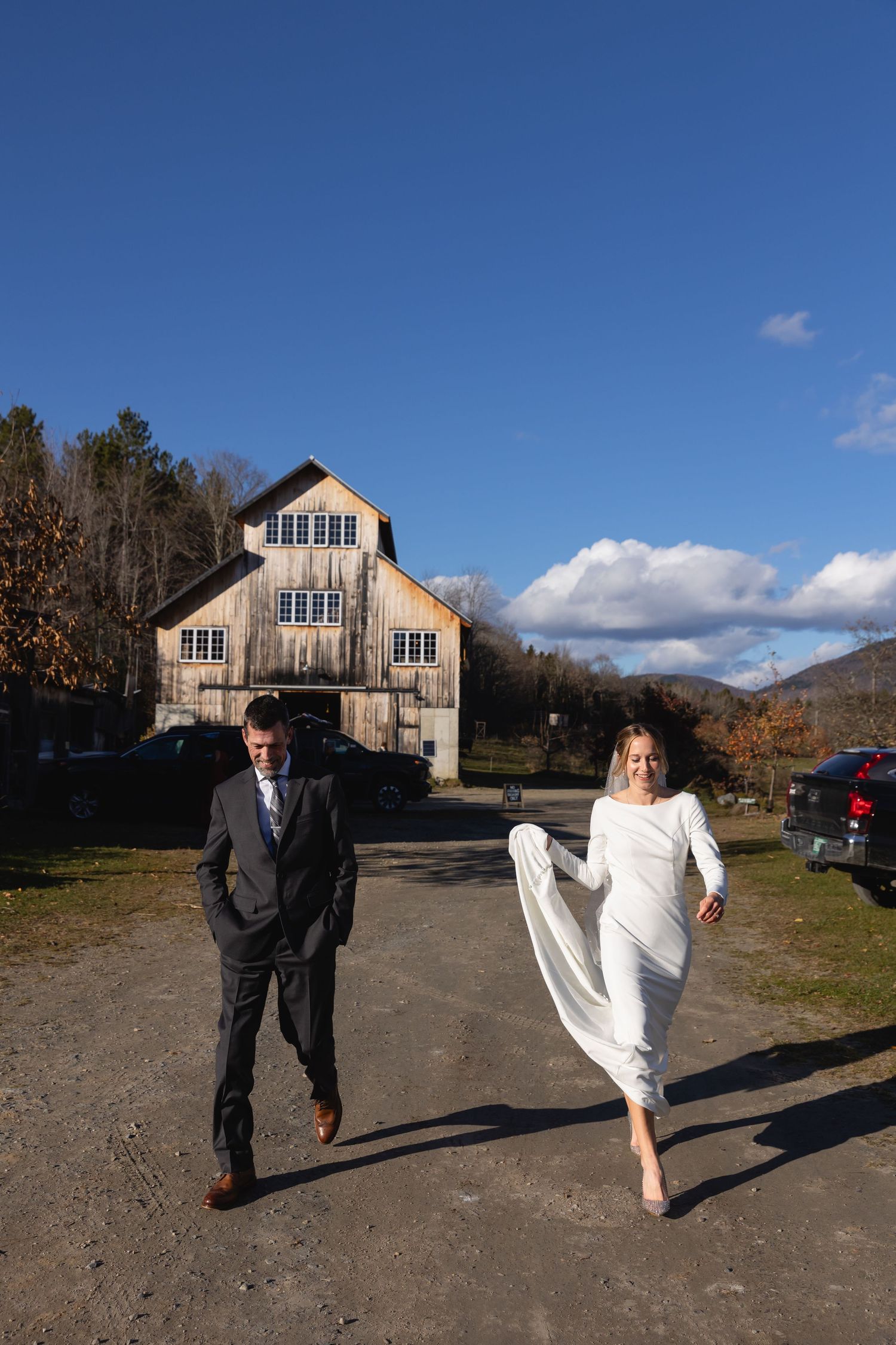 A couple walking outside a rustic barn venue on a sunny autumn day in the mountains.