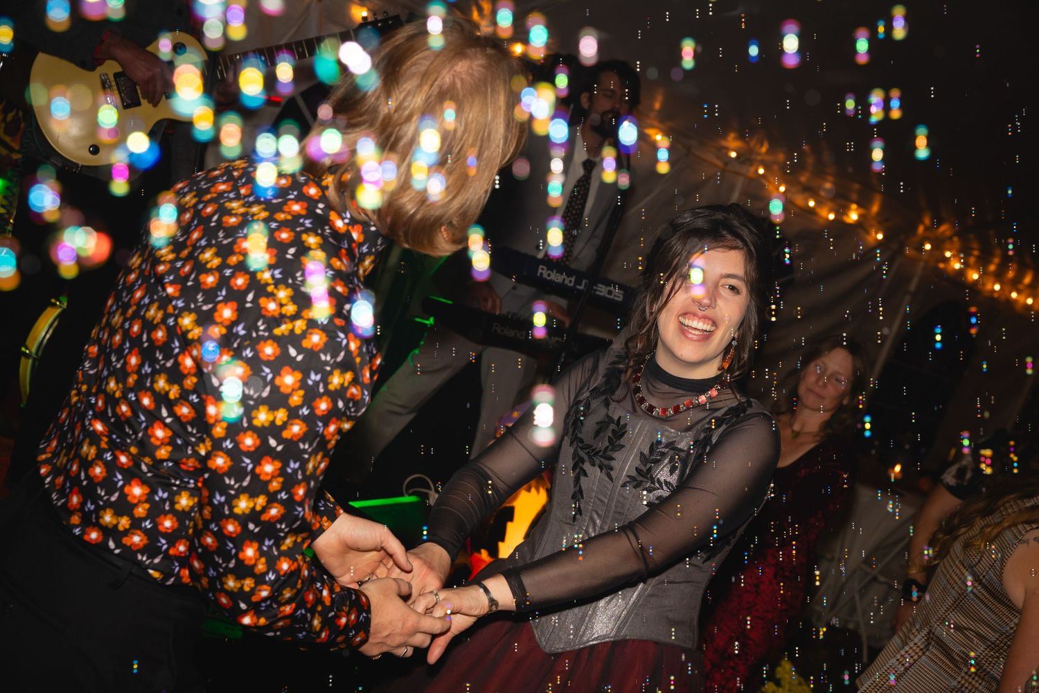 People dance and celebrate at a festive nighttime party with colorful lights and decorations overhead.