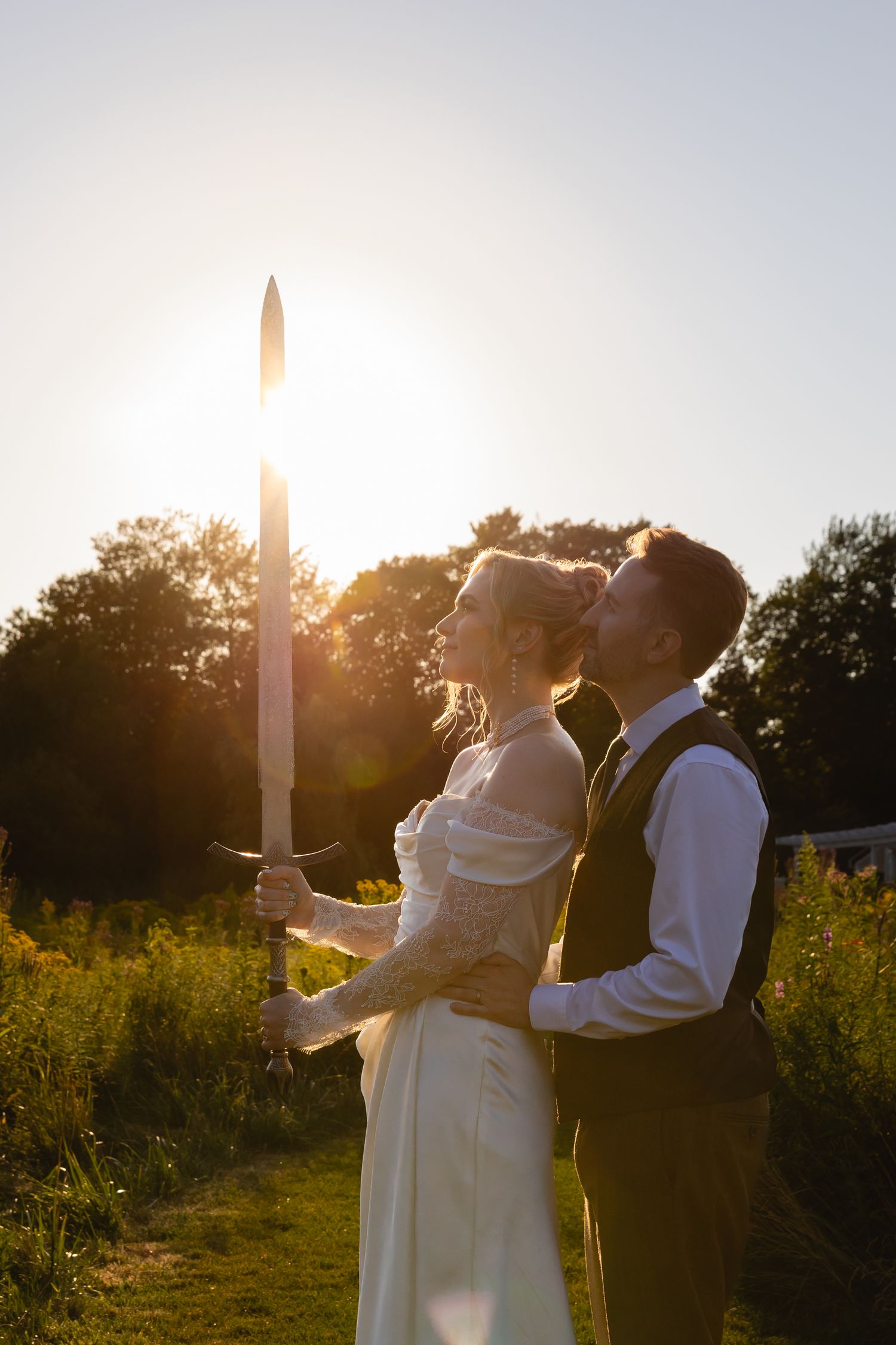 A couple shares an intimate moment in a sunlit field during sunset, with glowing candles creating a romantic atmosphere.