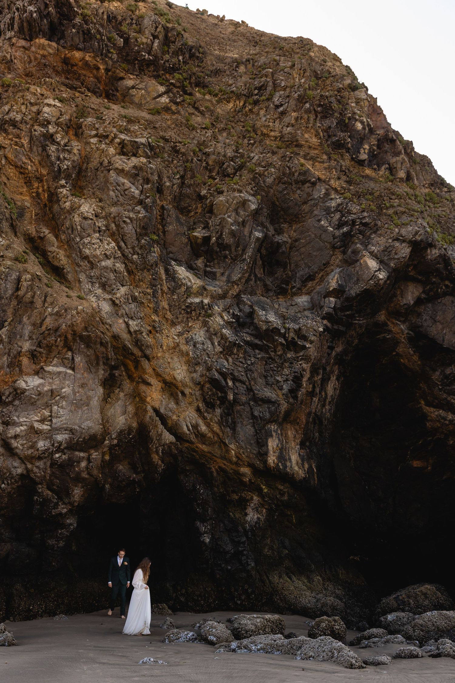 Dramatic coastal cave formations with dark rocky cliffs and overhanging rocks along a rugged beach at sunset.