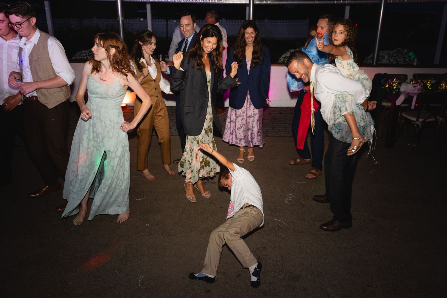 People dancing and celebrating at a lively wedding reception party on a dimly lit dance floor.