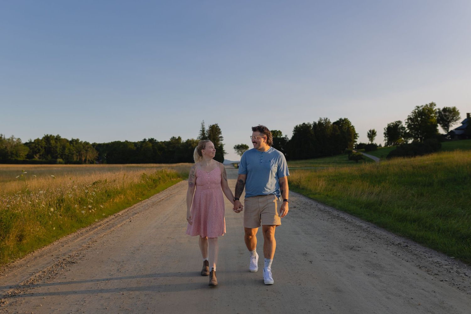 A couple takes an evening stroll down a rural dirt road surrounded by golden fields.