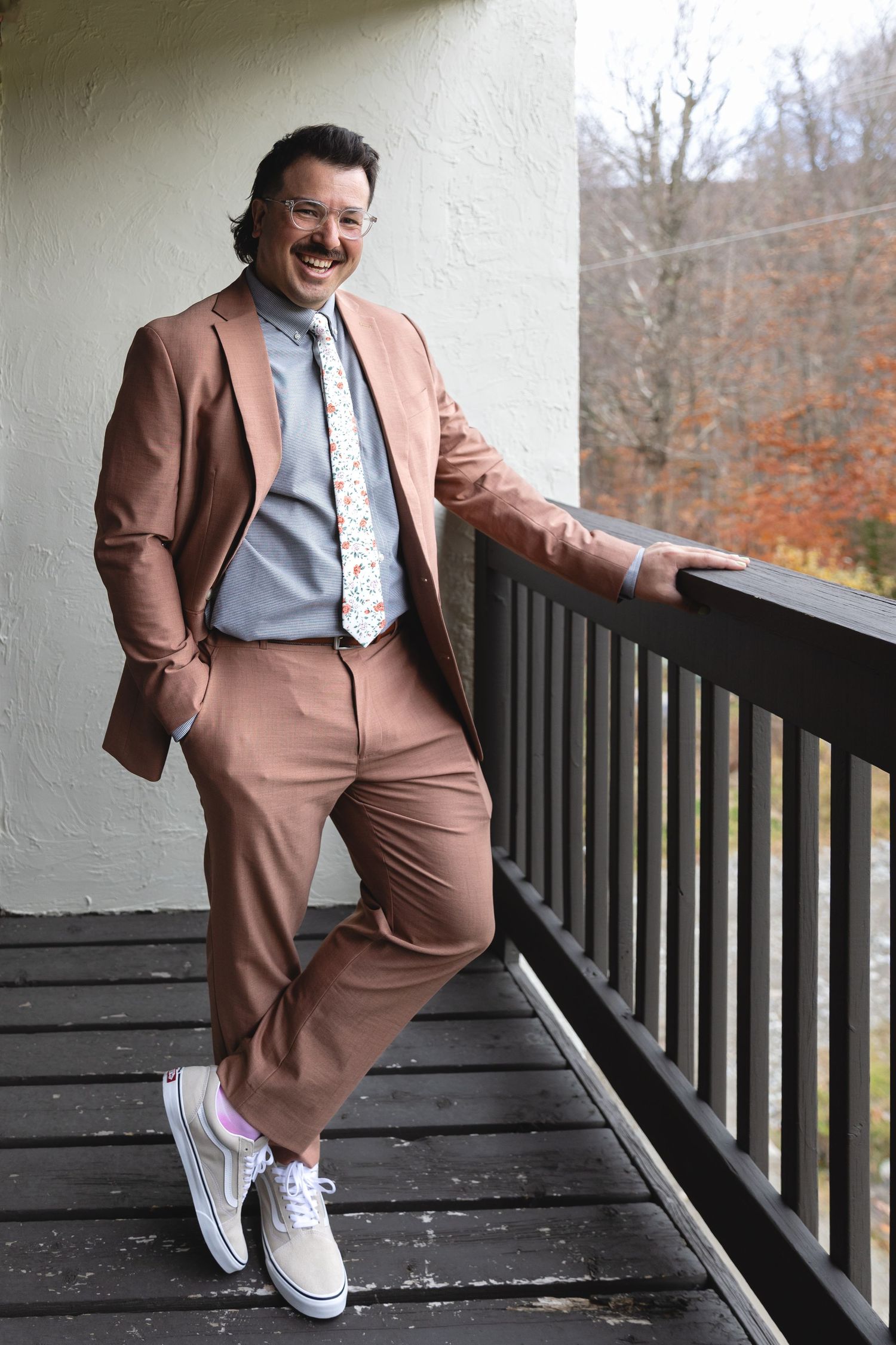 Individual wearing a brown suit with white sneakers poses casually on a deck.