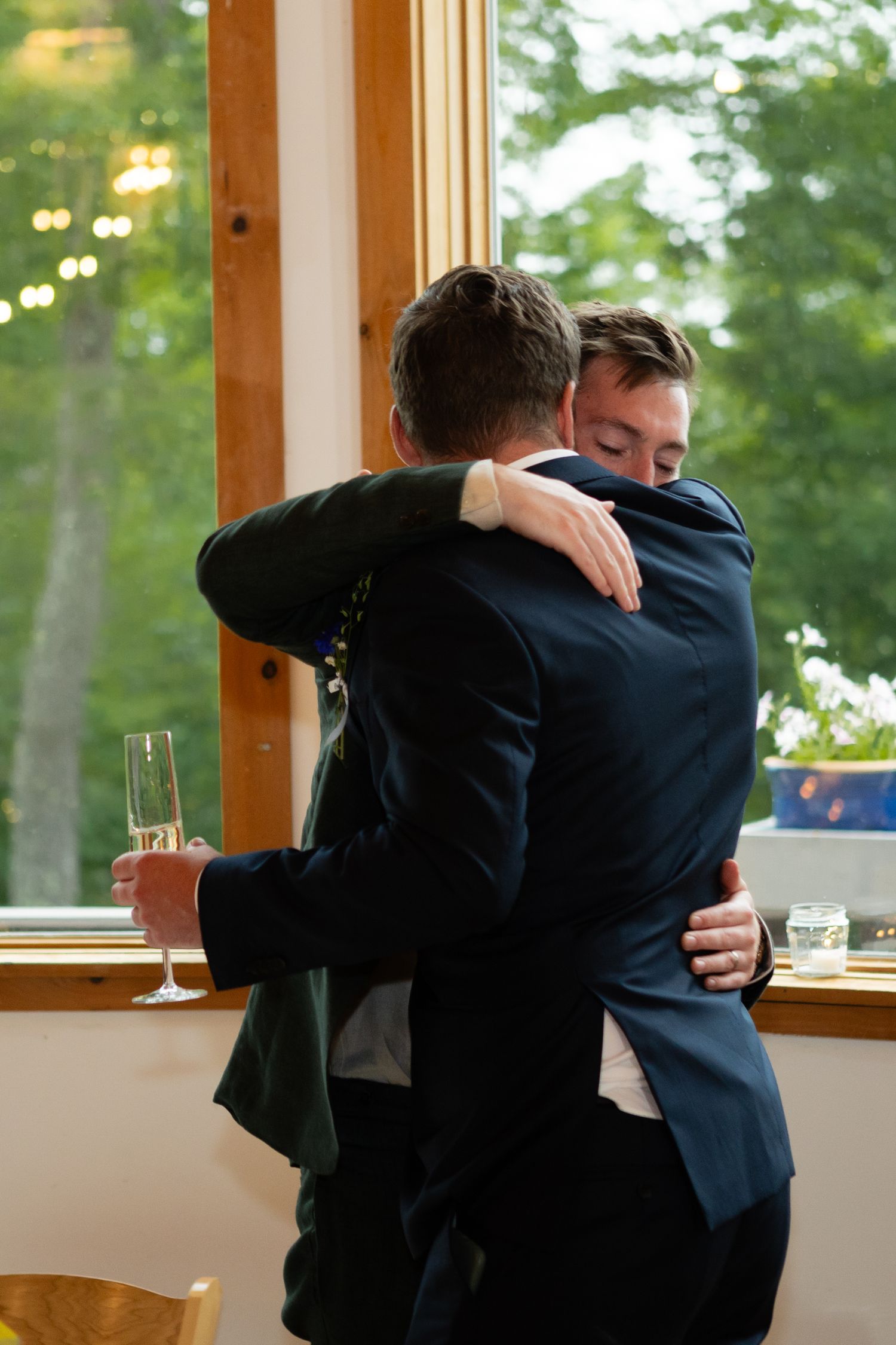 Two people in formal attire sharing an emotional embrace near a window.