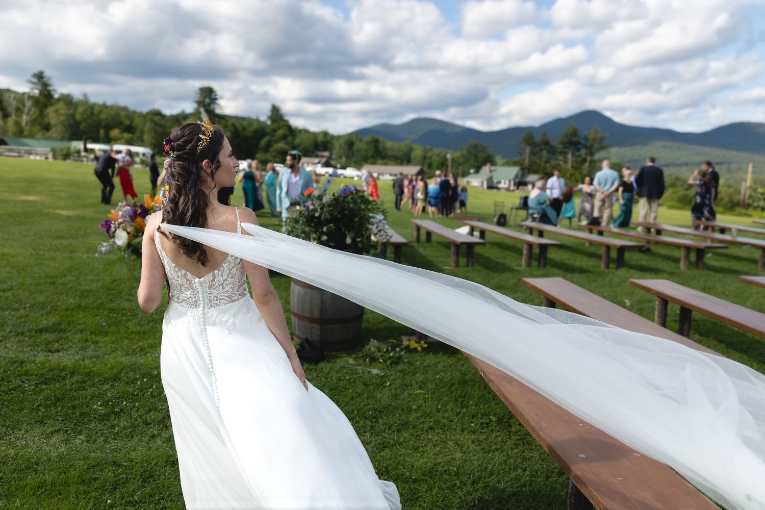 Person balancing on a wooden plank outdoors with mountains and cloudy sky in background.