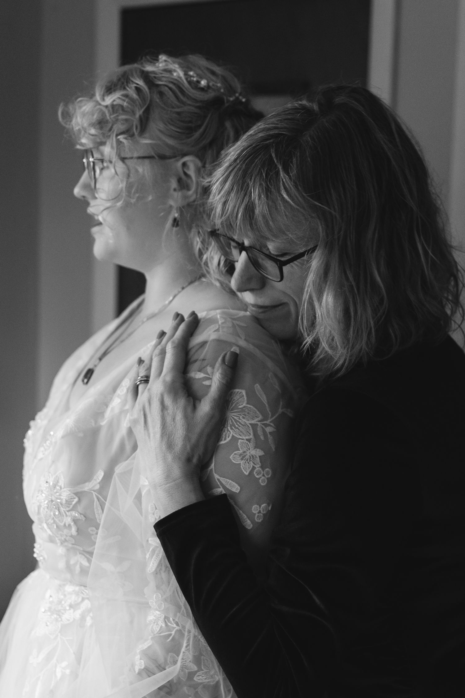 Black and white photo captures tender moment during wedding preparation.