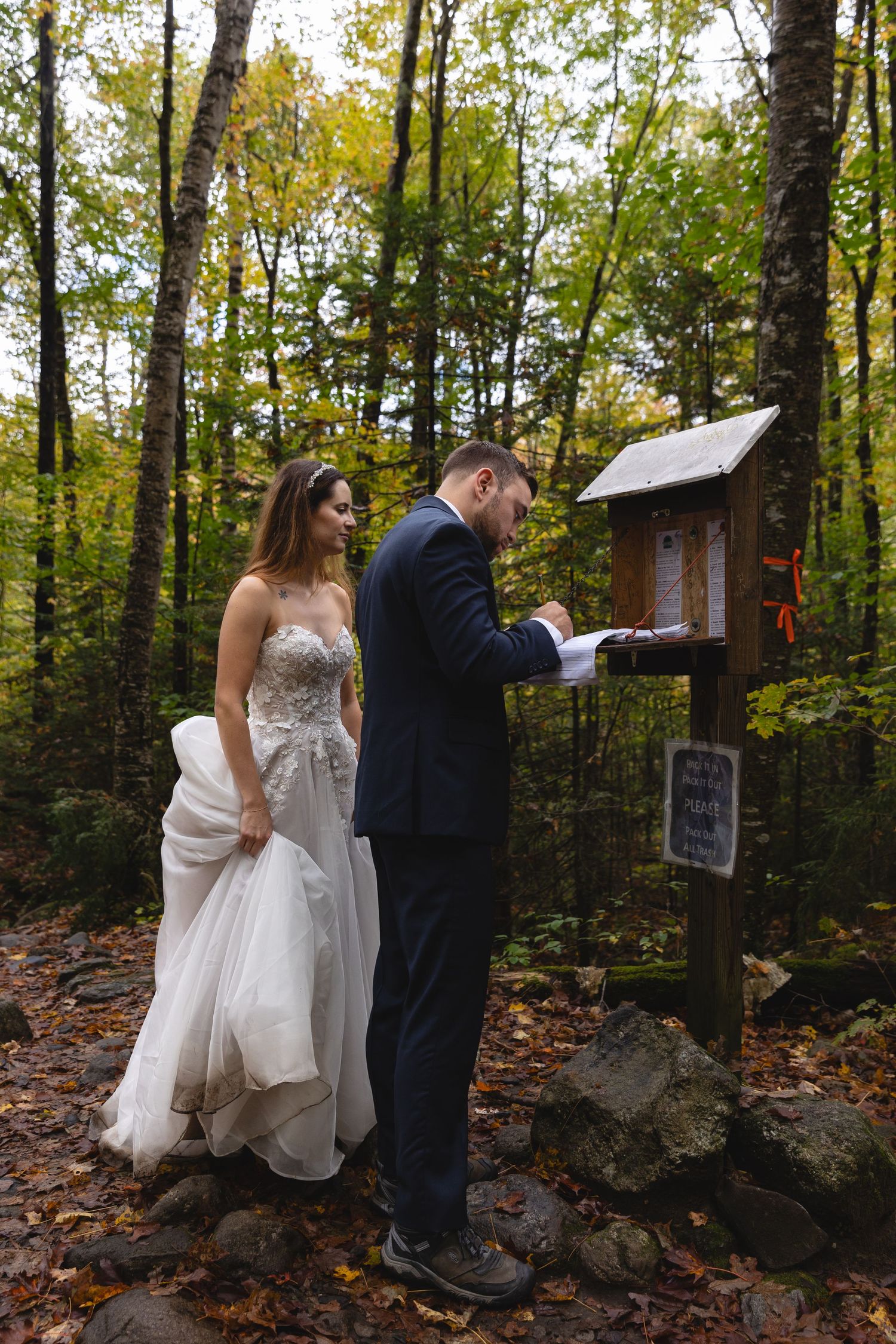 A couple signing a small wooden mailbox in an autumn forest setting.