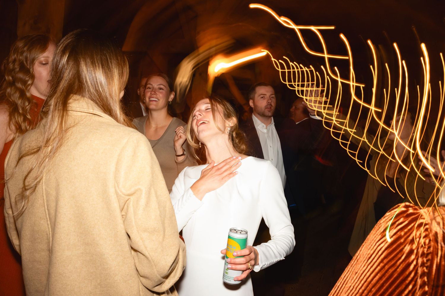 People dancing and socializing at a nightclub with glowing light trails creating wavy patterns in the background.