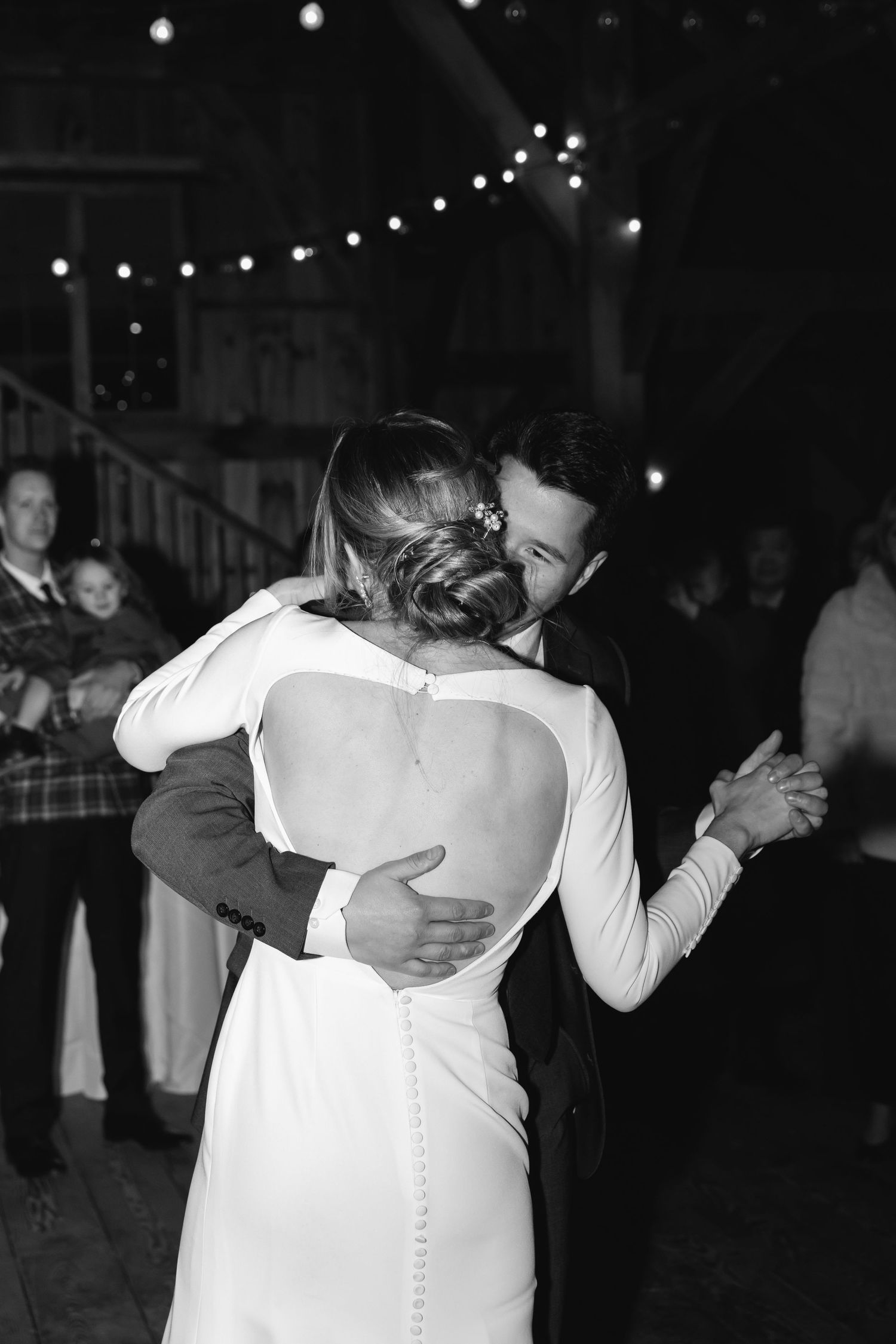 A romantic black and white wedding photo showing a couple sharing their first dance under twinkling string lights.