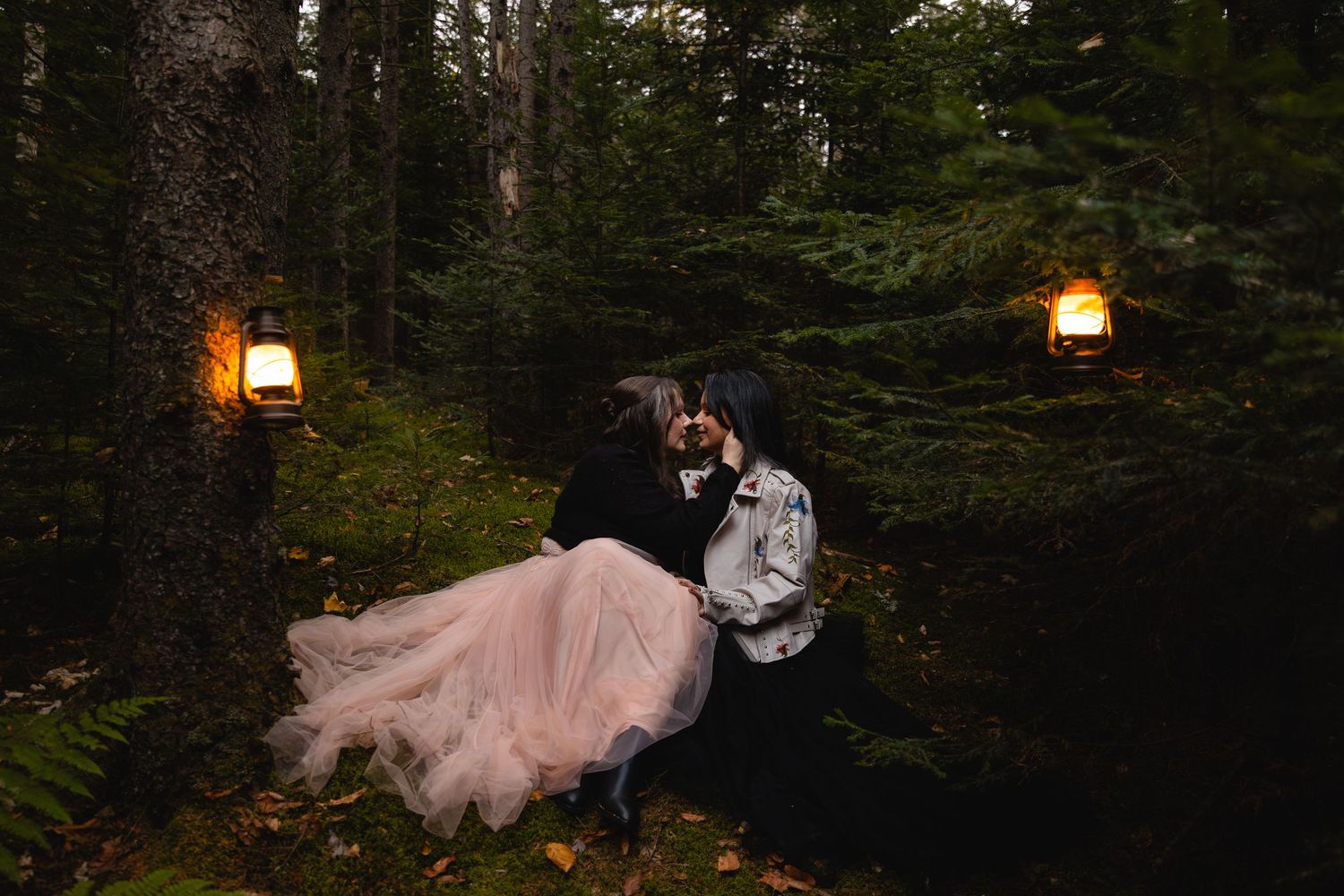 Couple sharing a kiss in a dark forest illuminated by two glowing lanterns hanging from trees.