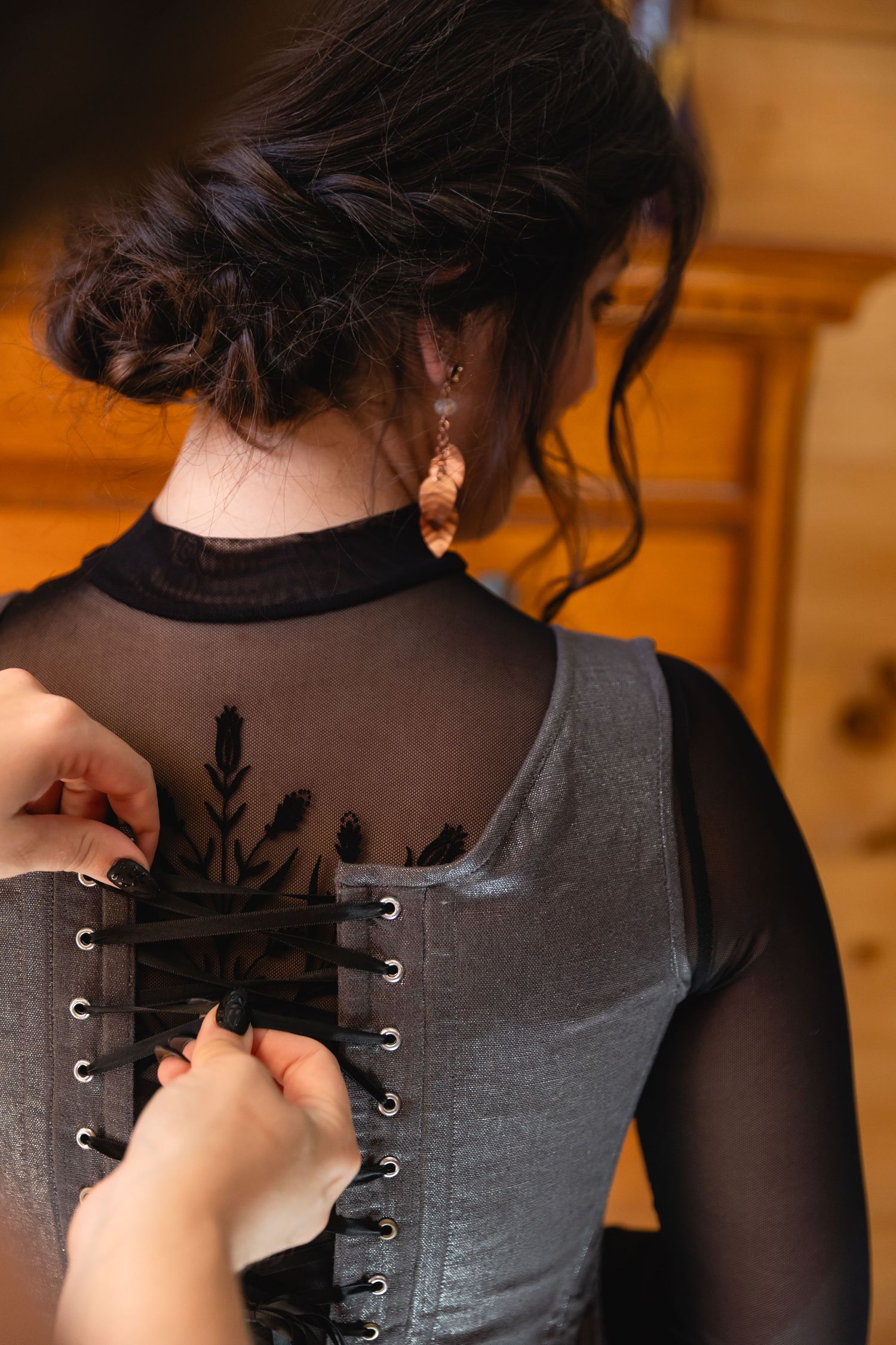 Close-up of hands lacing up a gray corset on a bride wearing a black sheer wedding dress.