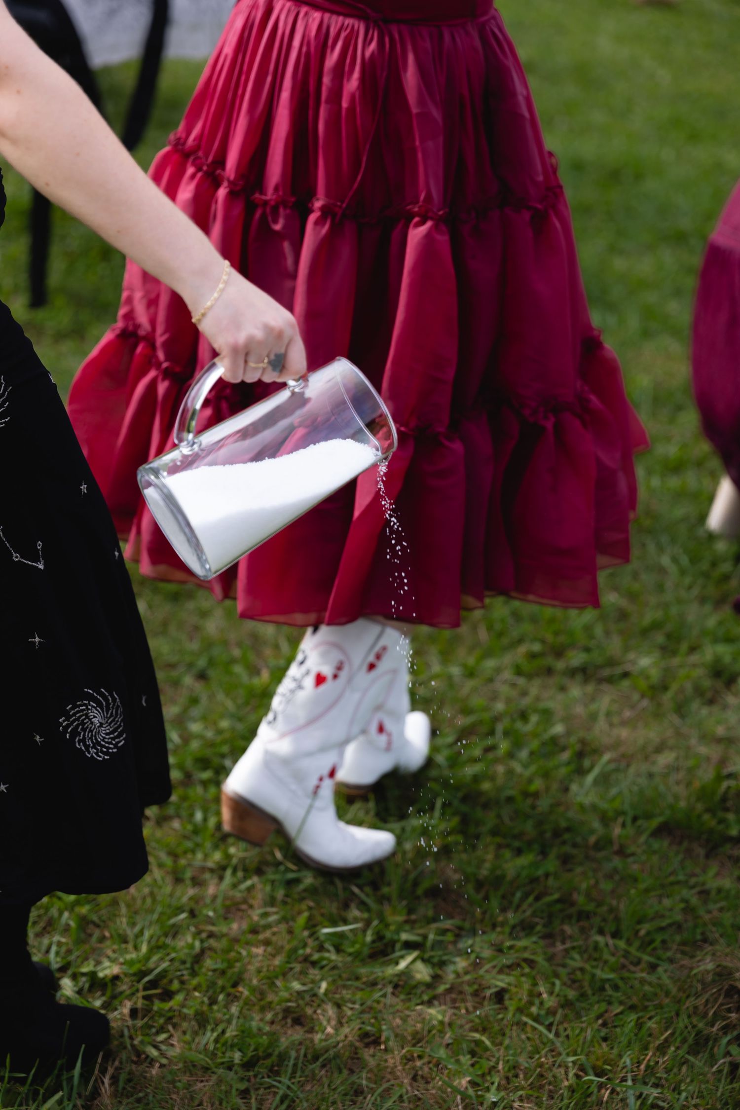 Flower girl in red ruffled dress and white cowboy boots during an outdoor wedding ceremony.