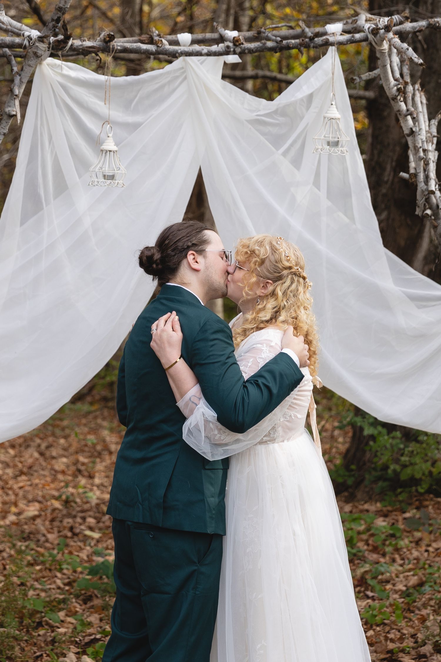 Intimate outdoor wedding ceremony with draped white fabric backdrop in autumn forest setting.
