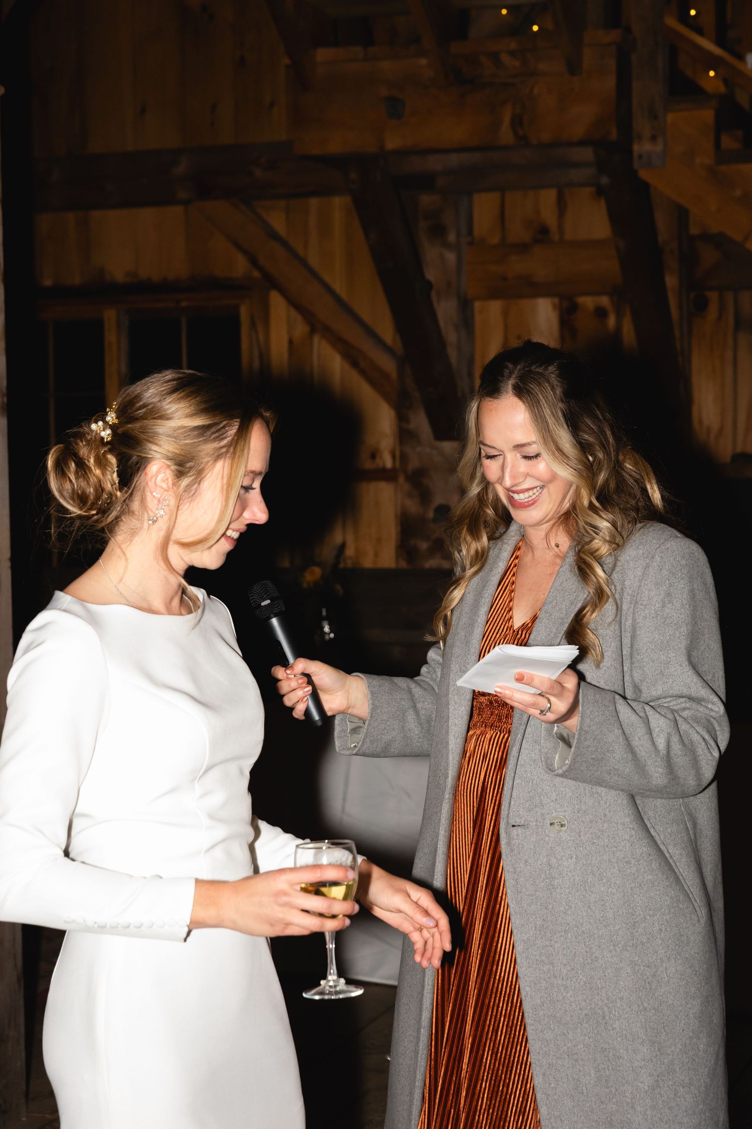 Two women in formal attire chatting and holding drinks at an indoor evening event.