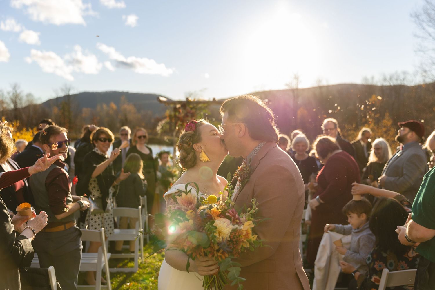 Wedding celebration with guests cheering in bright sunlight against a mountain backdrop.