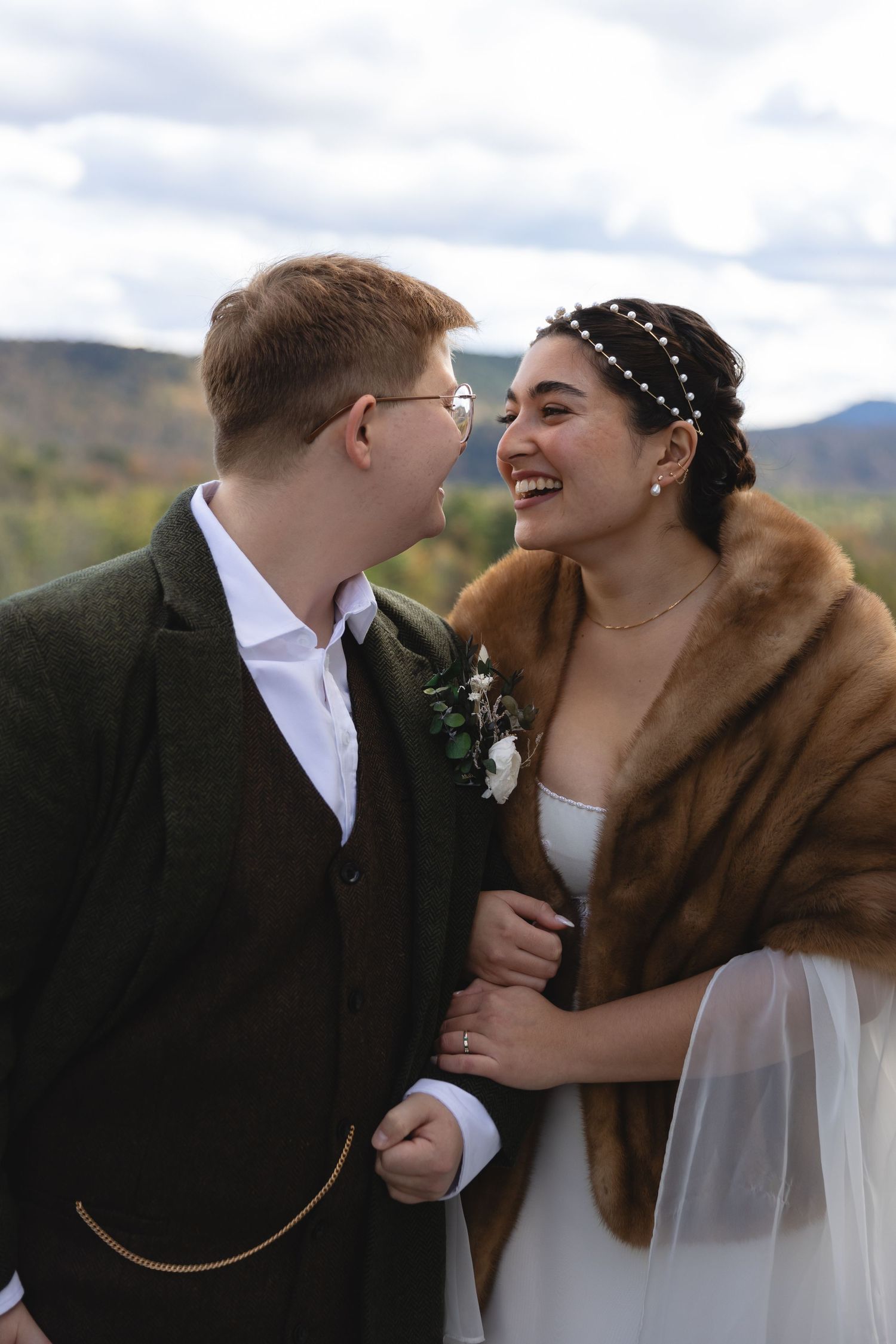 A joyful fall wedding moment featuring a bride in a fur stole and groom in dark jacket against a mountain backdrop.