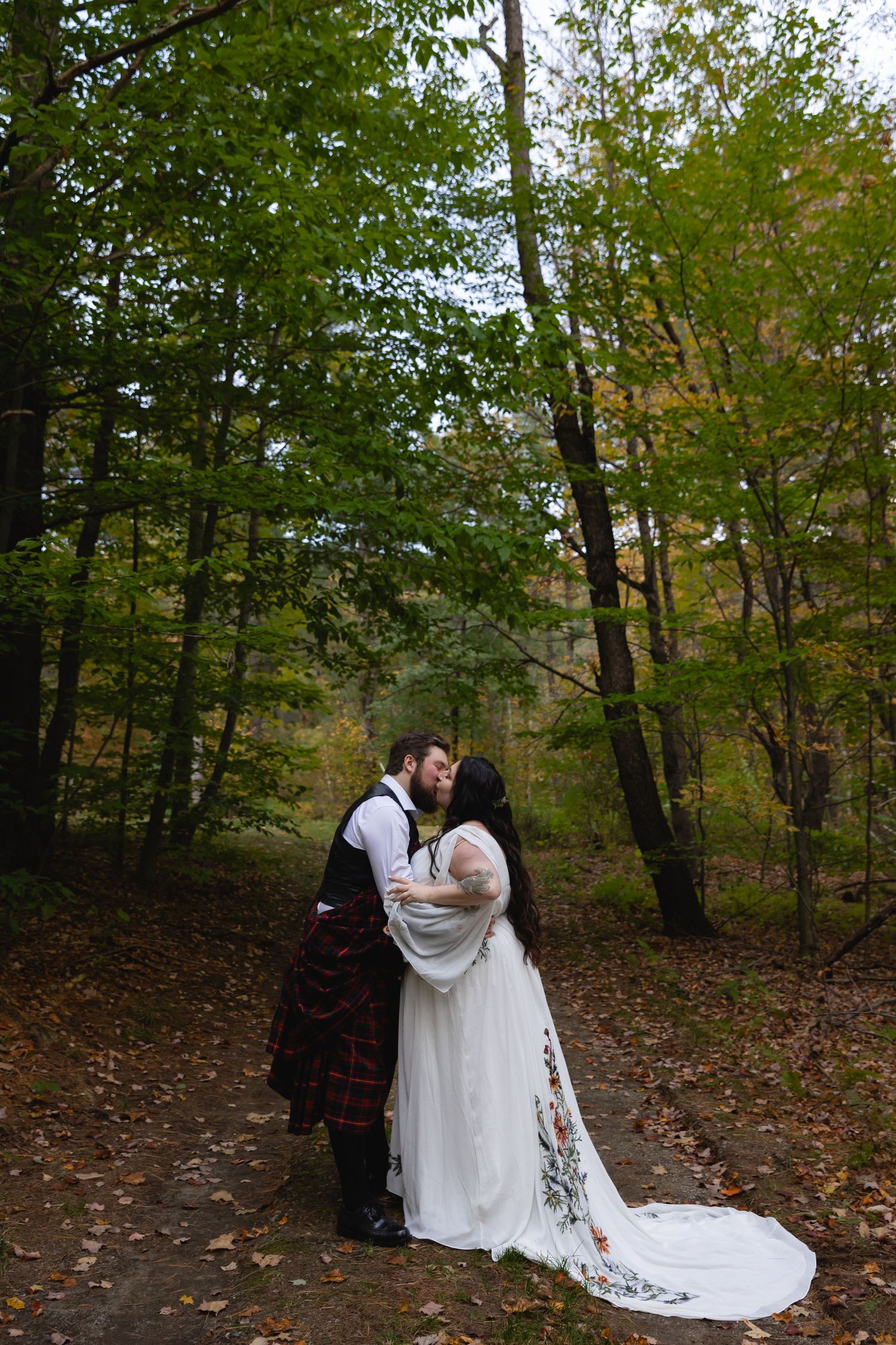 A couple shares an intimate moment in traditional Celtic wedding attire against a forest backdrop.