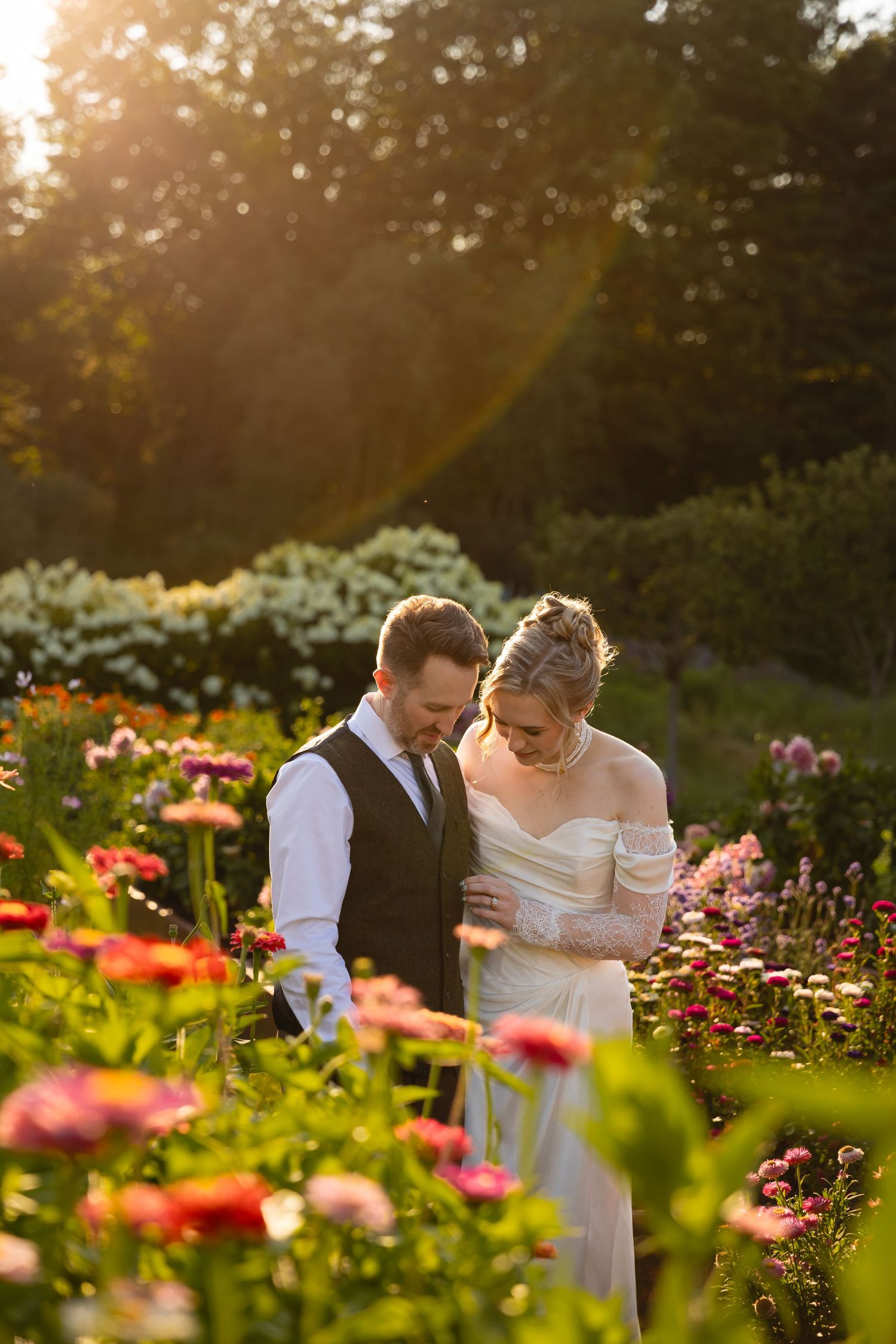 A couple shares an intimate moment in a vibrant garden of pink and orange flowers at golden hour.