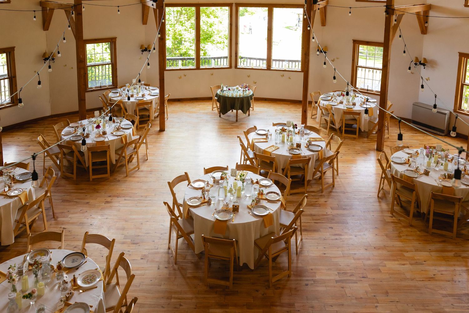 Rustic wedding reception venue with wooden cross-back chairs and round tables set for an elegant celebration.