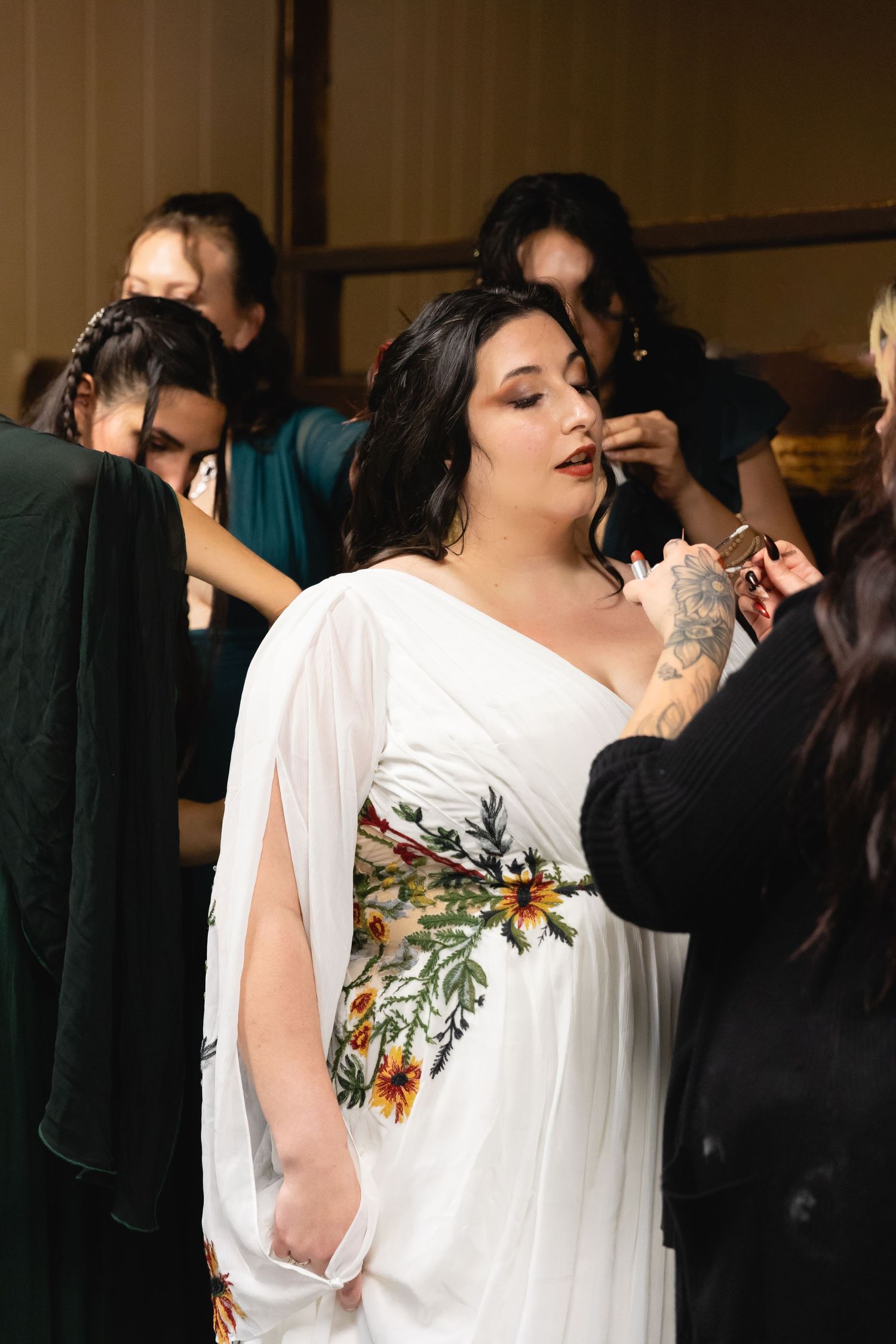 Bride in white floral dress getting final makeup touches during wedding preparations.