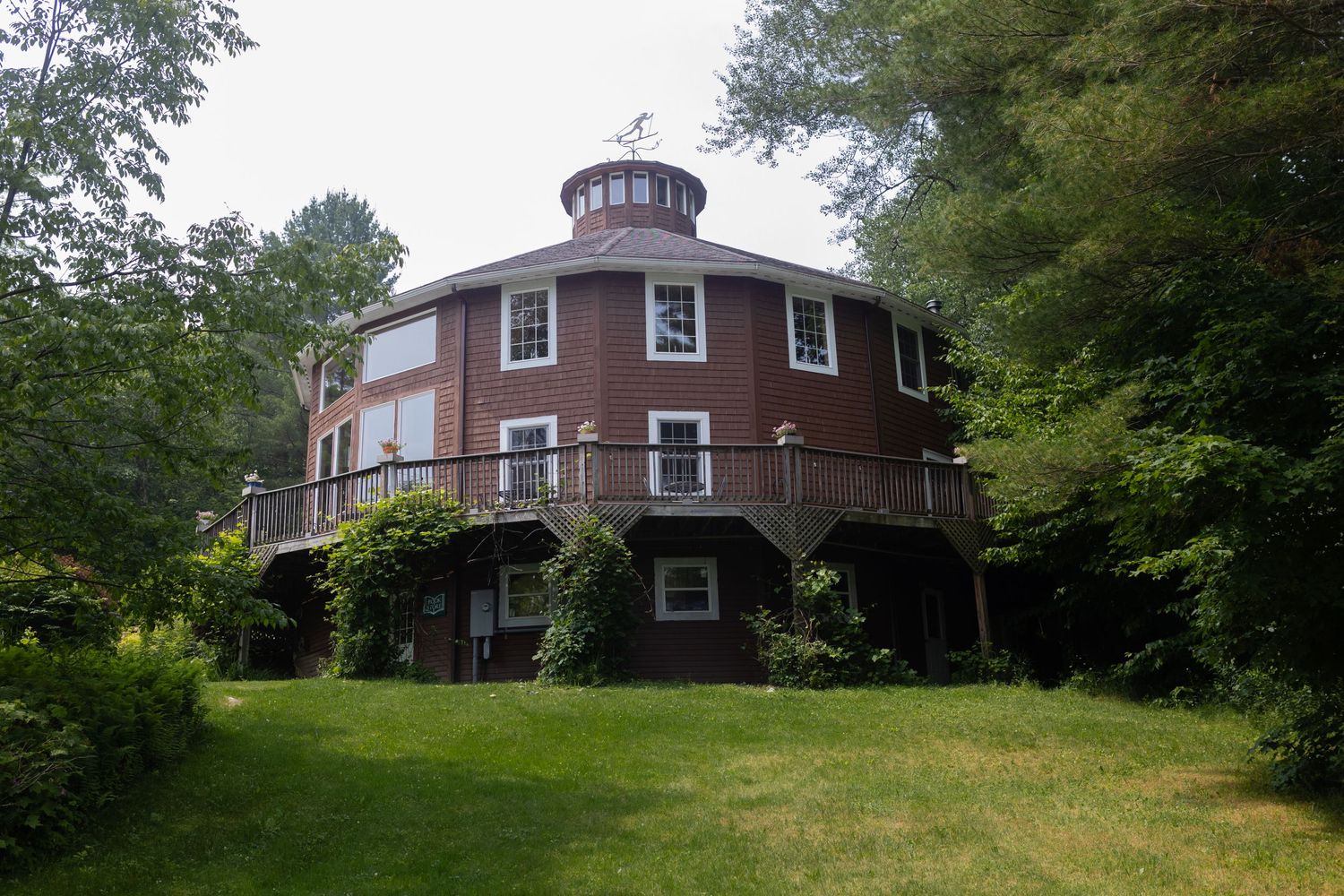 A unique round brick house with a domed roof surrounded by lush green trees and landscaping.