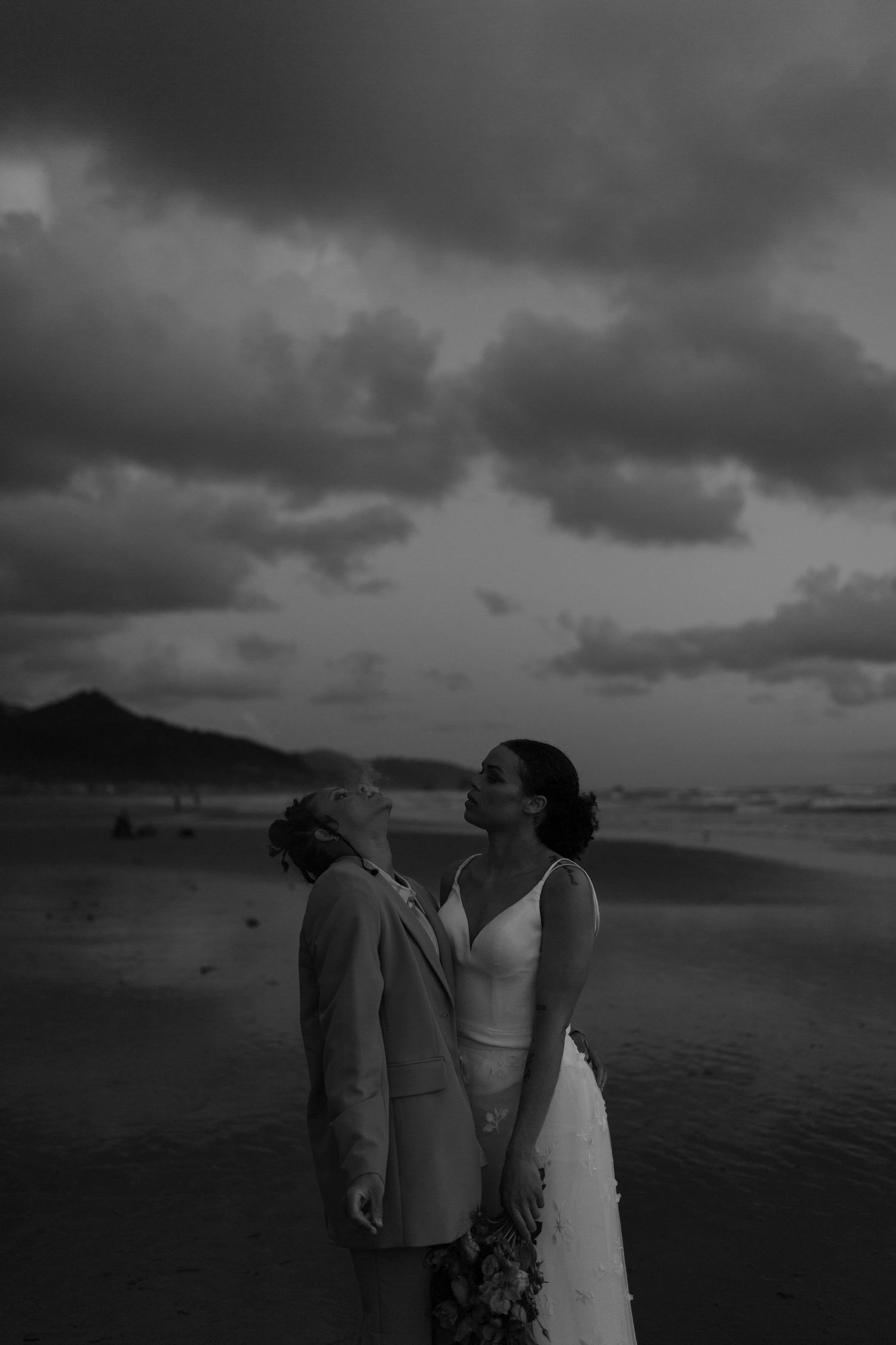 A dramatic black and white beach photo with stormy clouds and two figures in silhouette.