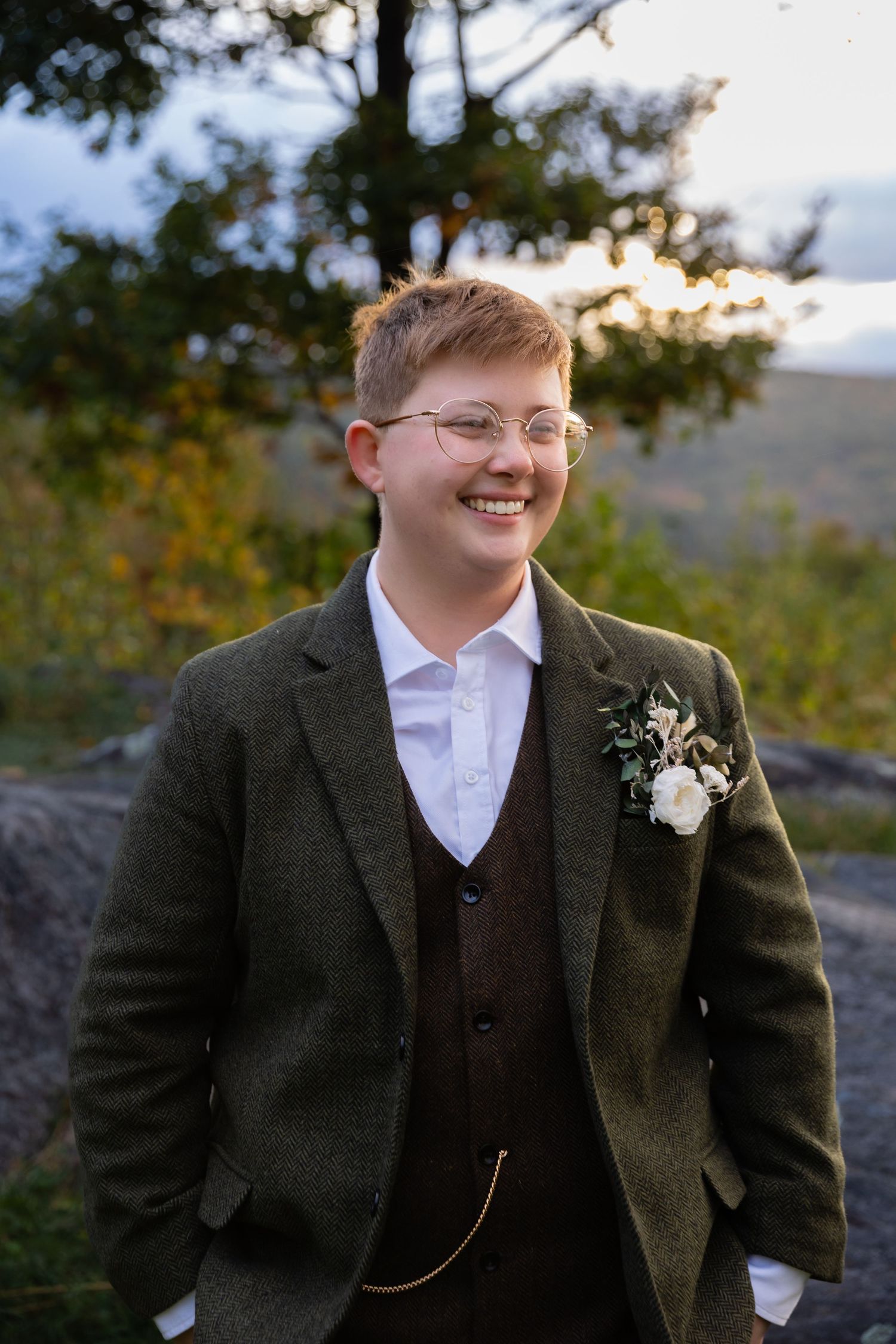 Portrait of a wedding party member in a three-piece suit and glasses outdoors at sunset.