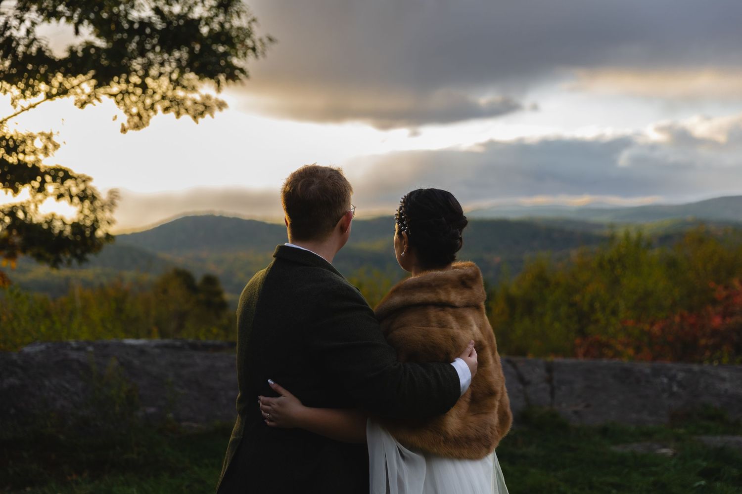 Couple embraces while overlooking mountain vista at sunset on their wedding day.
