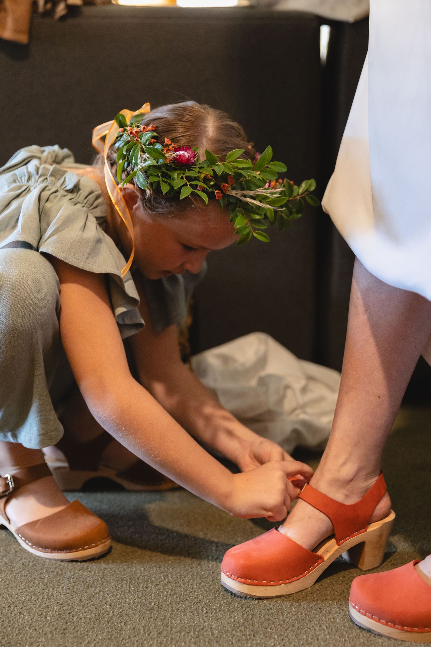 Person wearing floral crown helps with coral-colored shoes.