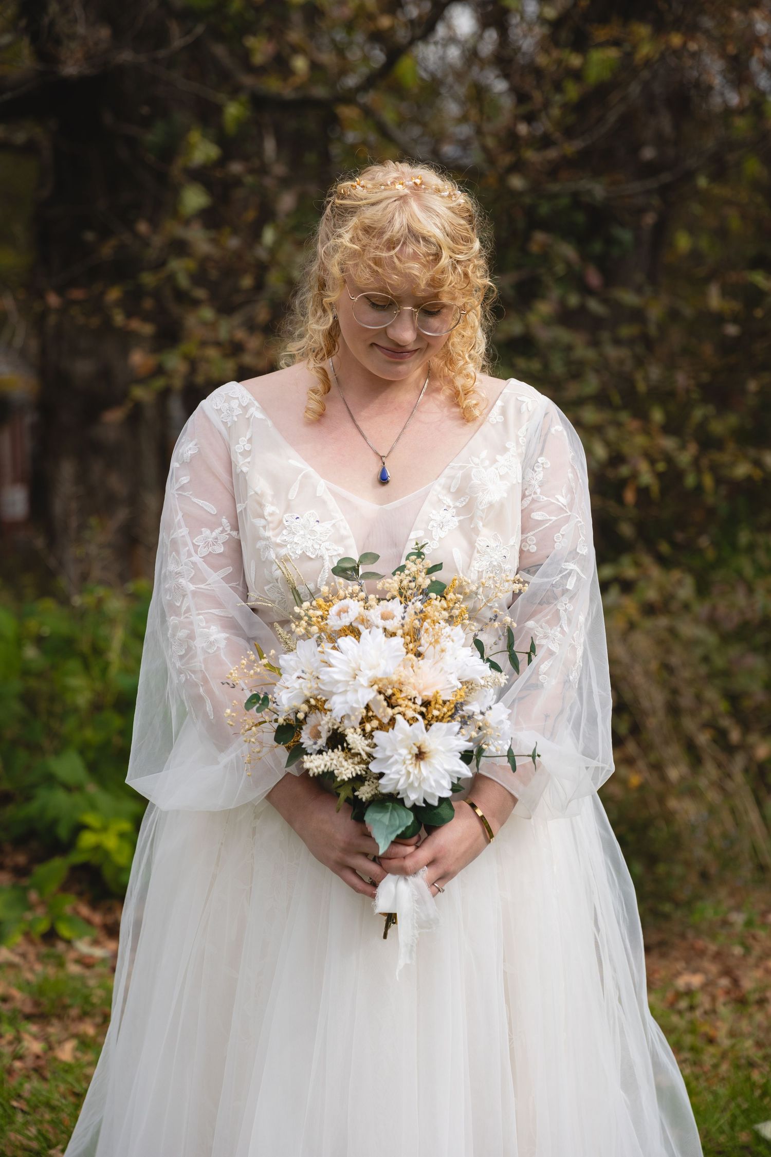 A bride in a white lace wedding dress with billowing sleeves holds a bouquet of white and yellow flowers.