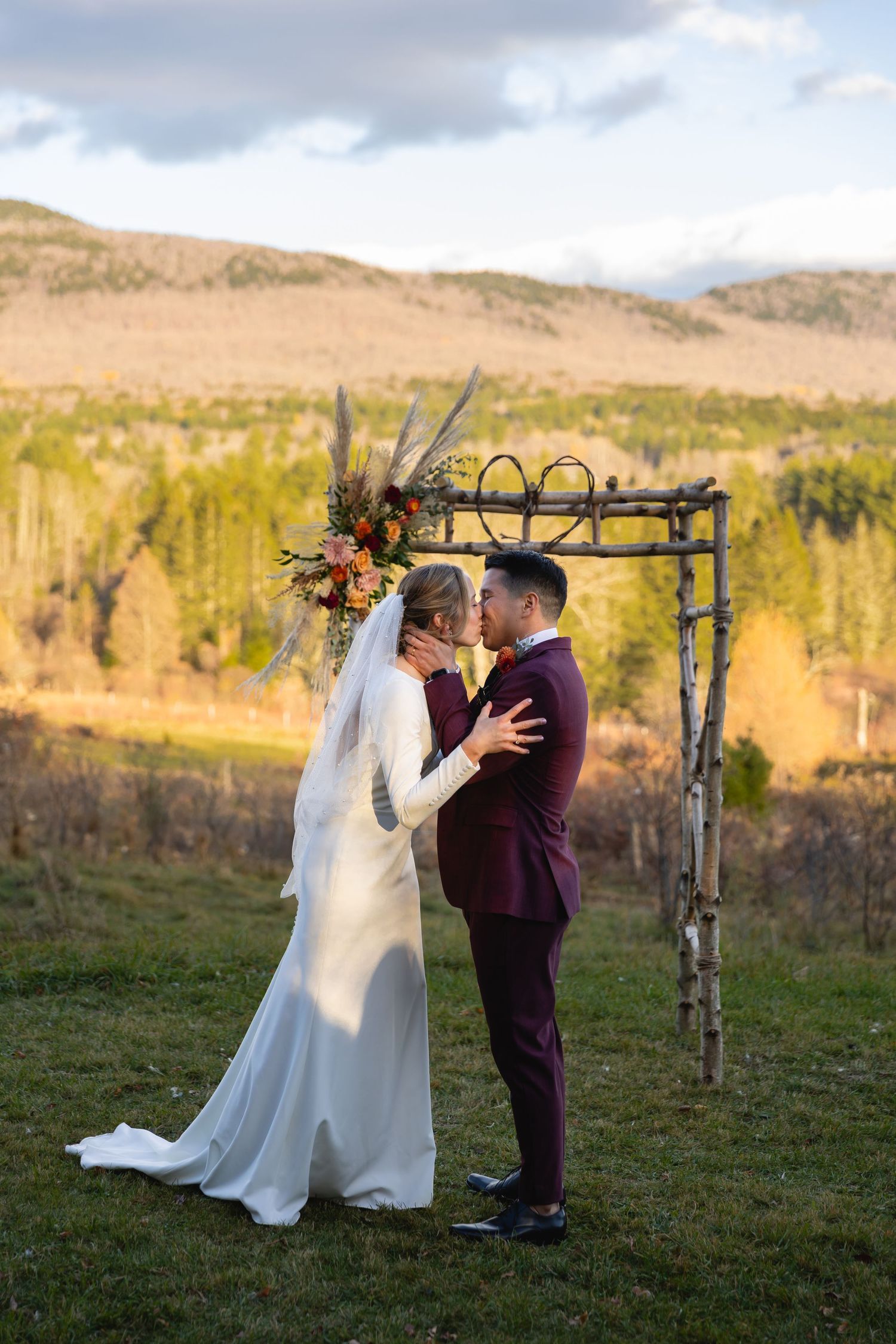 A couple shares a romantic moment under a rustic wooden arch during an autumn wedding ceremony in the mountains.