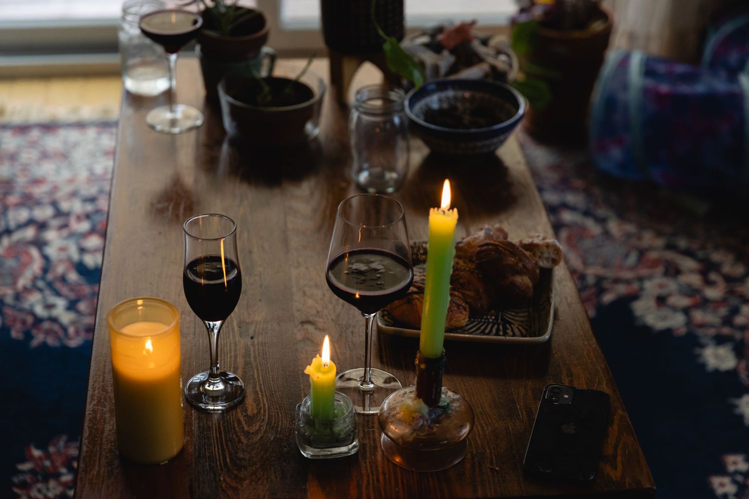 Moody table setting with glowing candles and wine glasses on a wooden surface over a patterned rug.