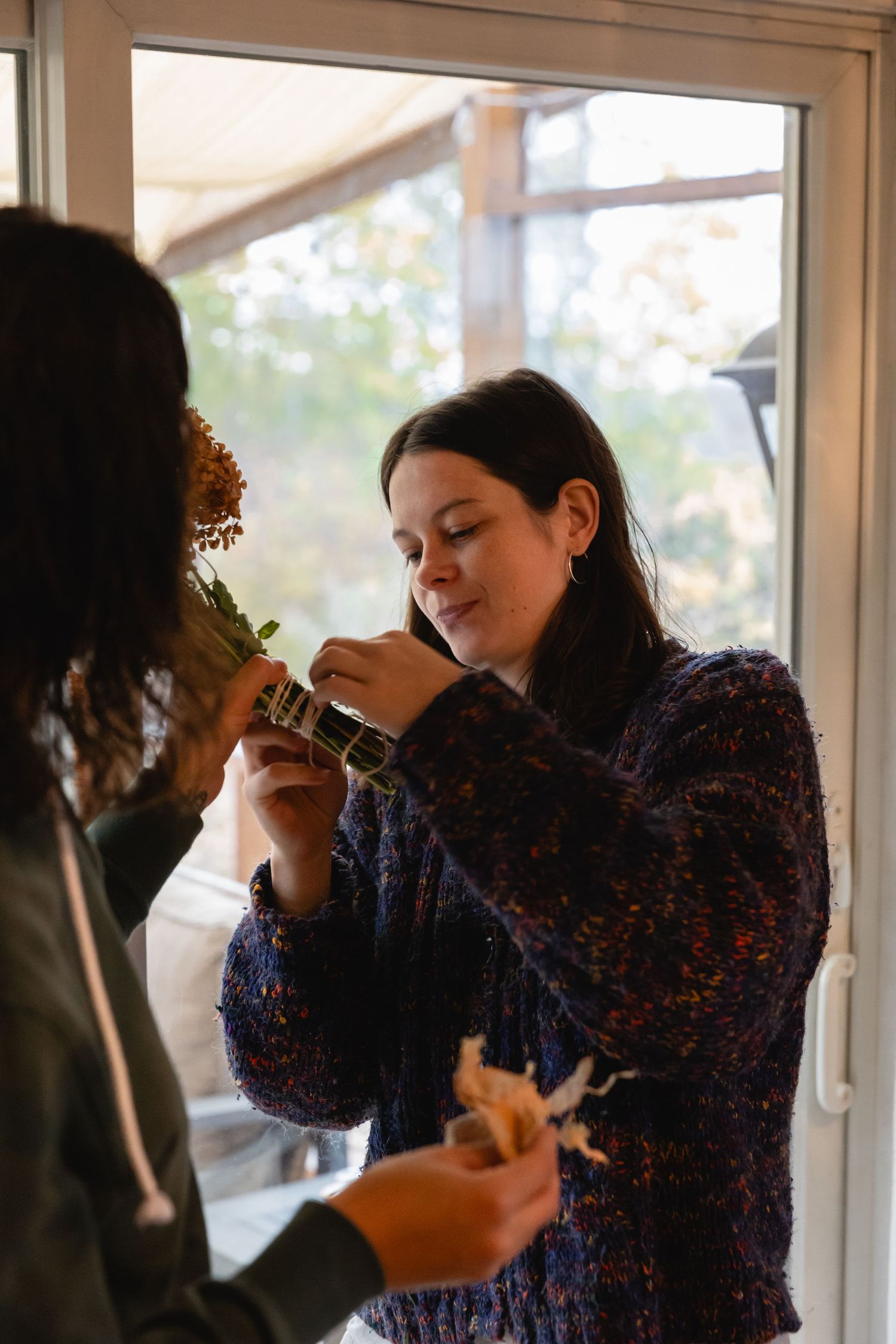 Someone wearing a blue patterned sweater takes a photo with a camera near a window in warm indoor lighting.