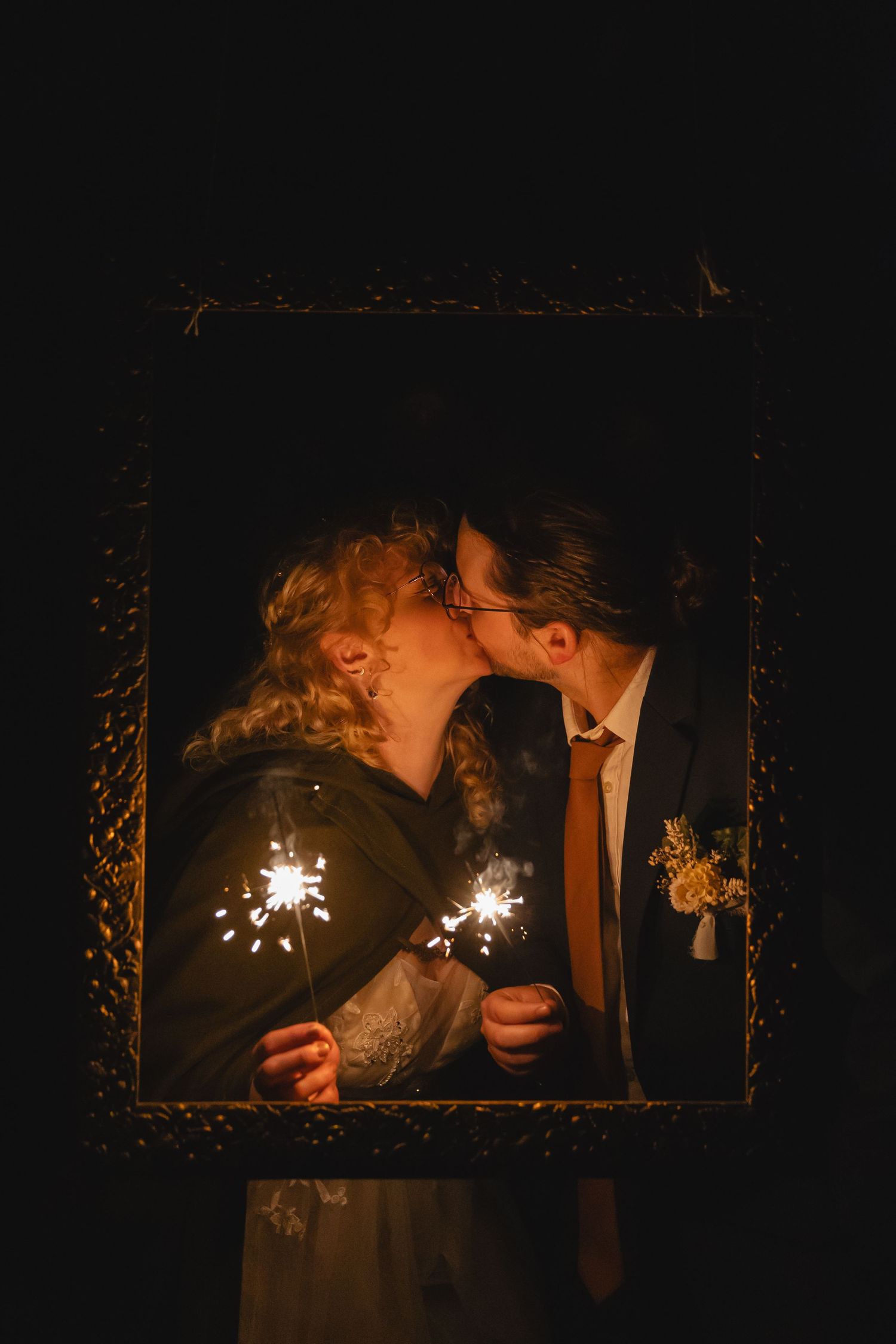Romantic sparkler moment through vintage frame at nighttime wedding celebration.