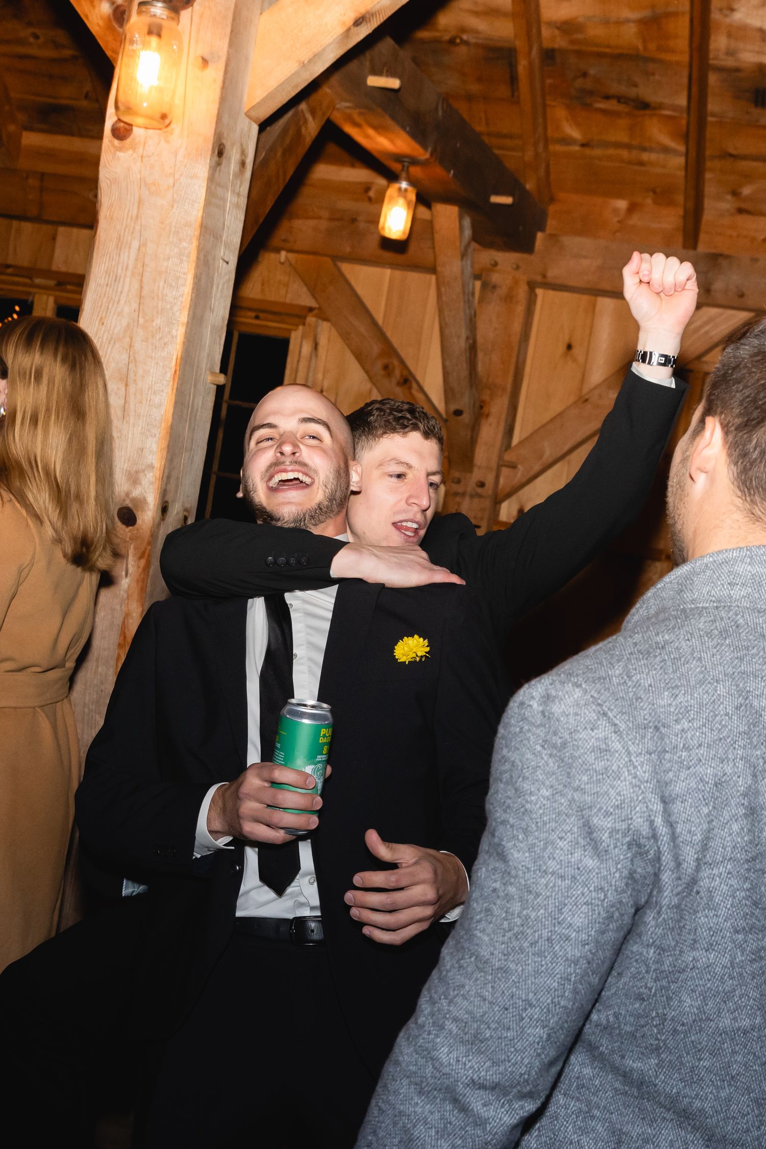 People celebrate and dance together at a rustic wooden venue with warm lighting and mason jar lamps.