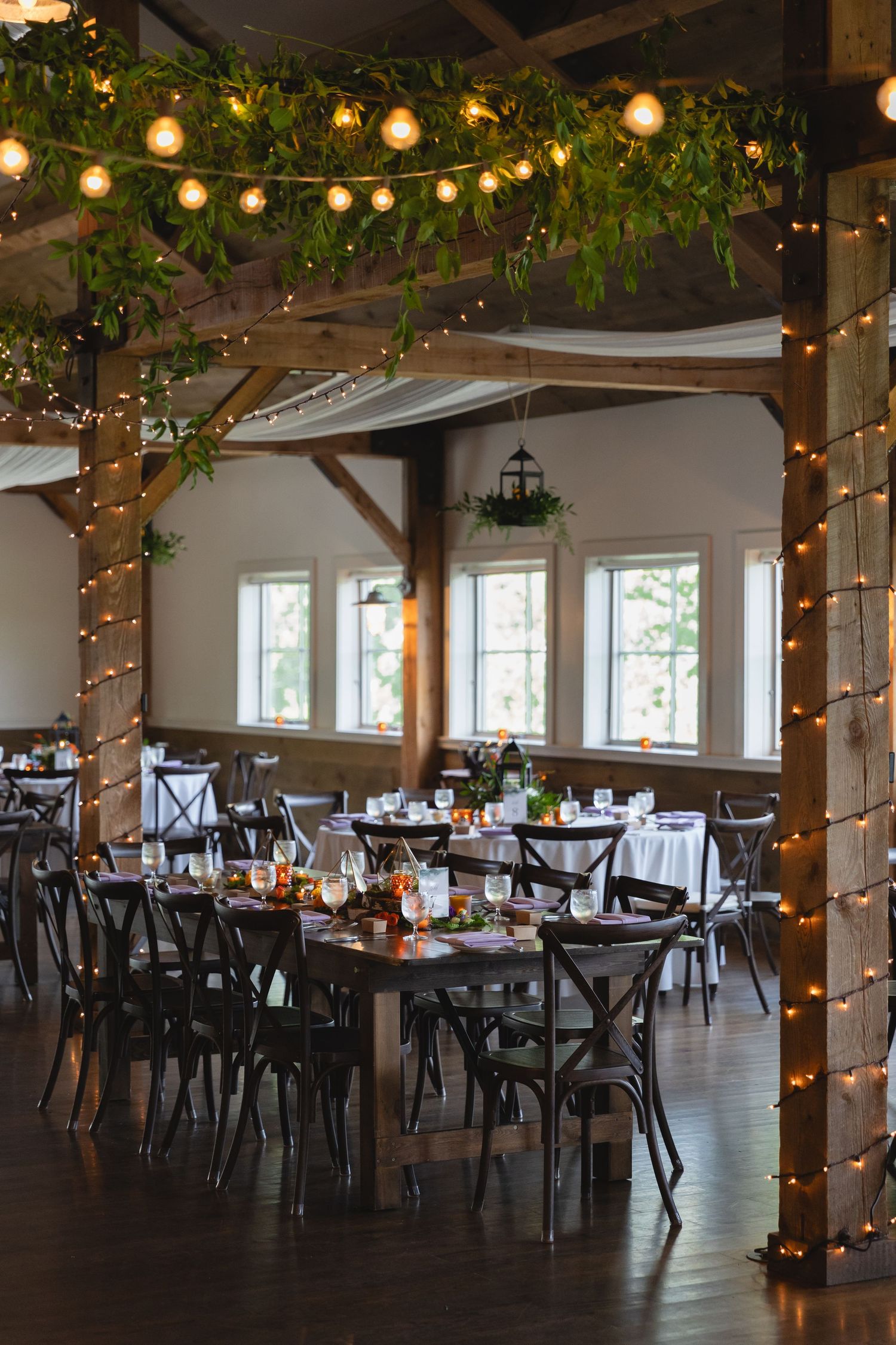 Rustic reception hall with wooden beams, string lights, and greenery decorations.