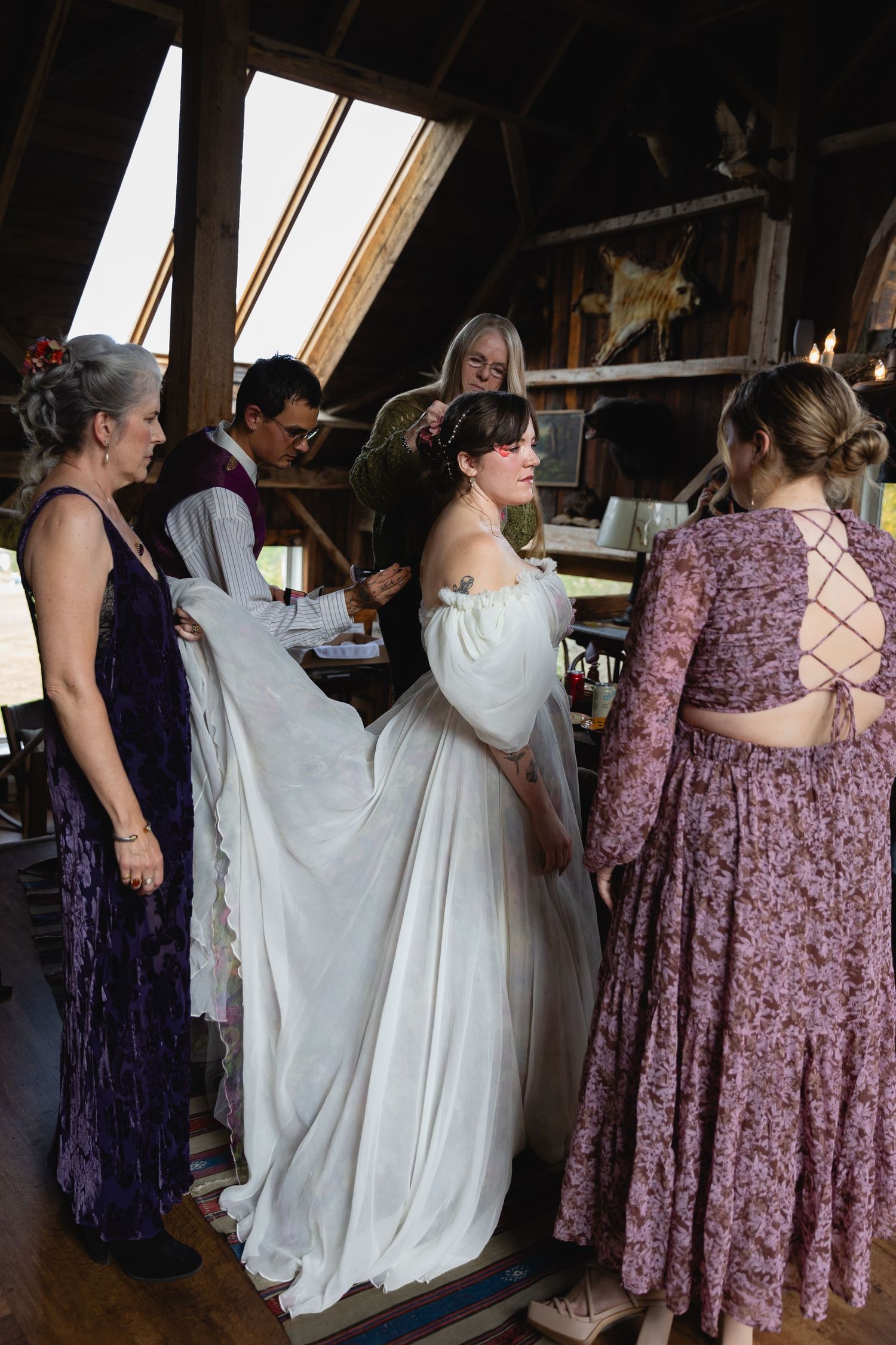 A group of people wearing formal attire gather in a rustic room with slanted ceiling and skylights.