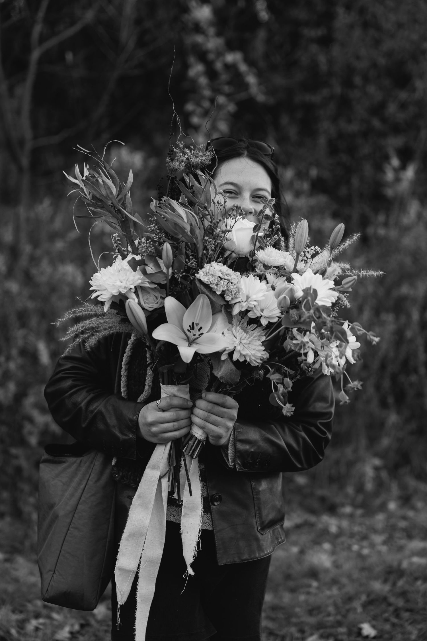 Black and white photo of someone in a leather jacket holding a beautiful floral bouquet with lilies and white flowers.