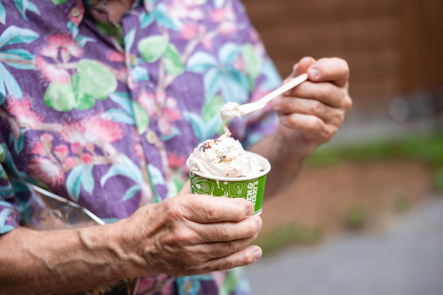 Someone wearing a floral shirt holds a cupcake with green frosting and sprinkles in a paper wrapper.