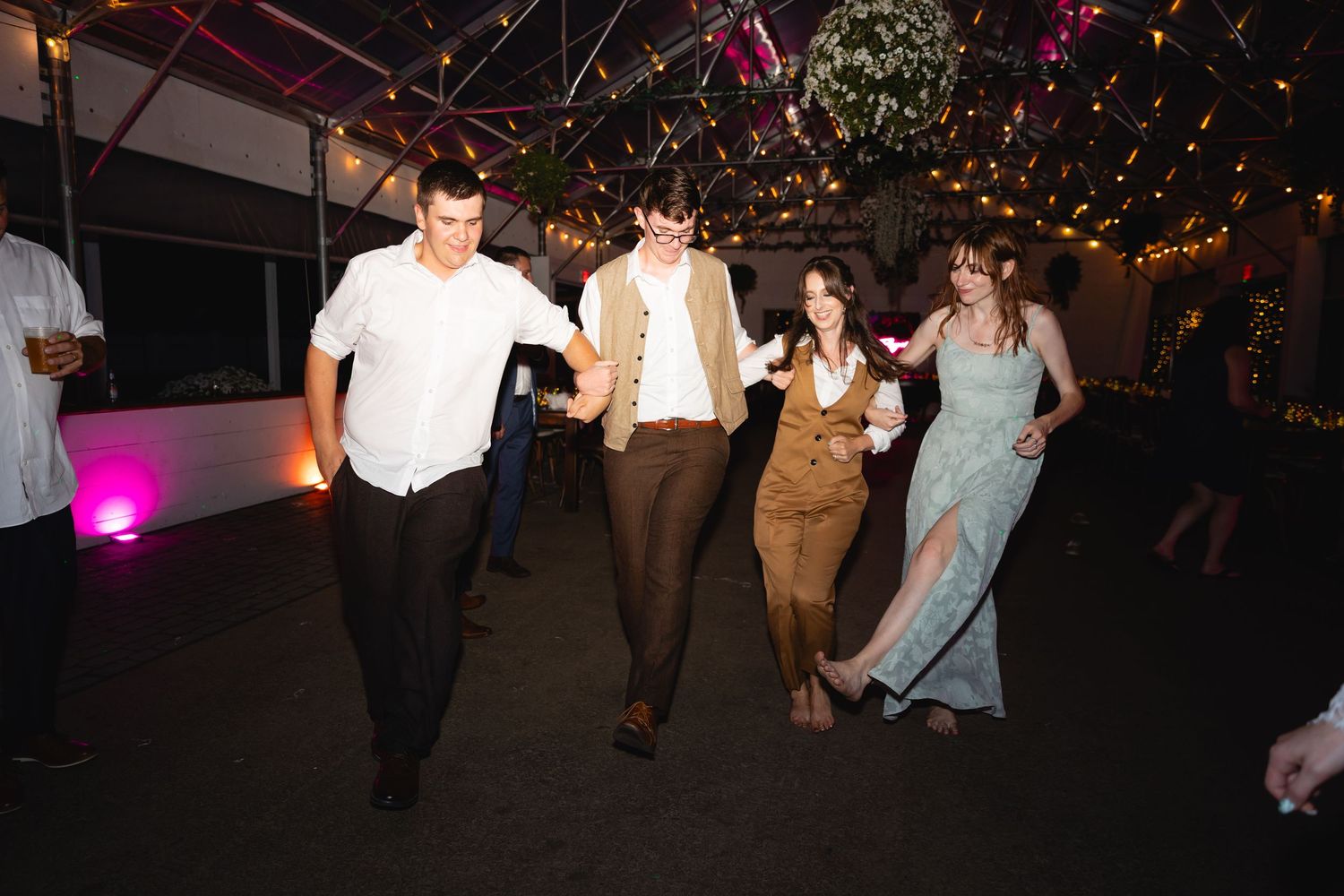 Wedding guests dance and celebrate on a dimly lit dance floor with colorful lighting and party atmosphere.