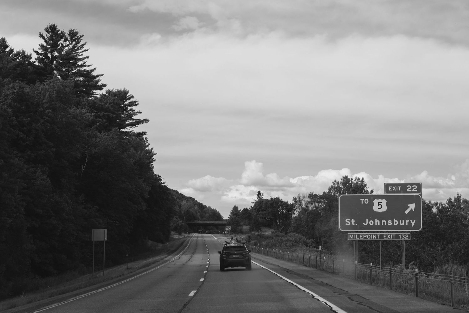 A series of black and white highway road signs and directional markers along a rural interstate.