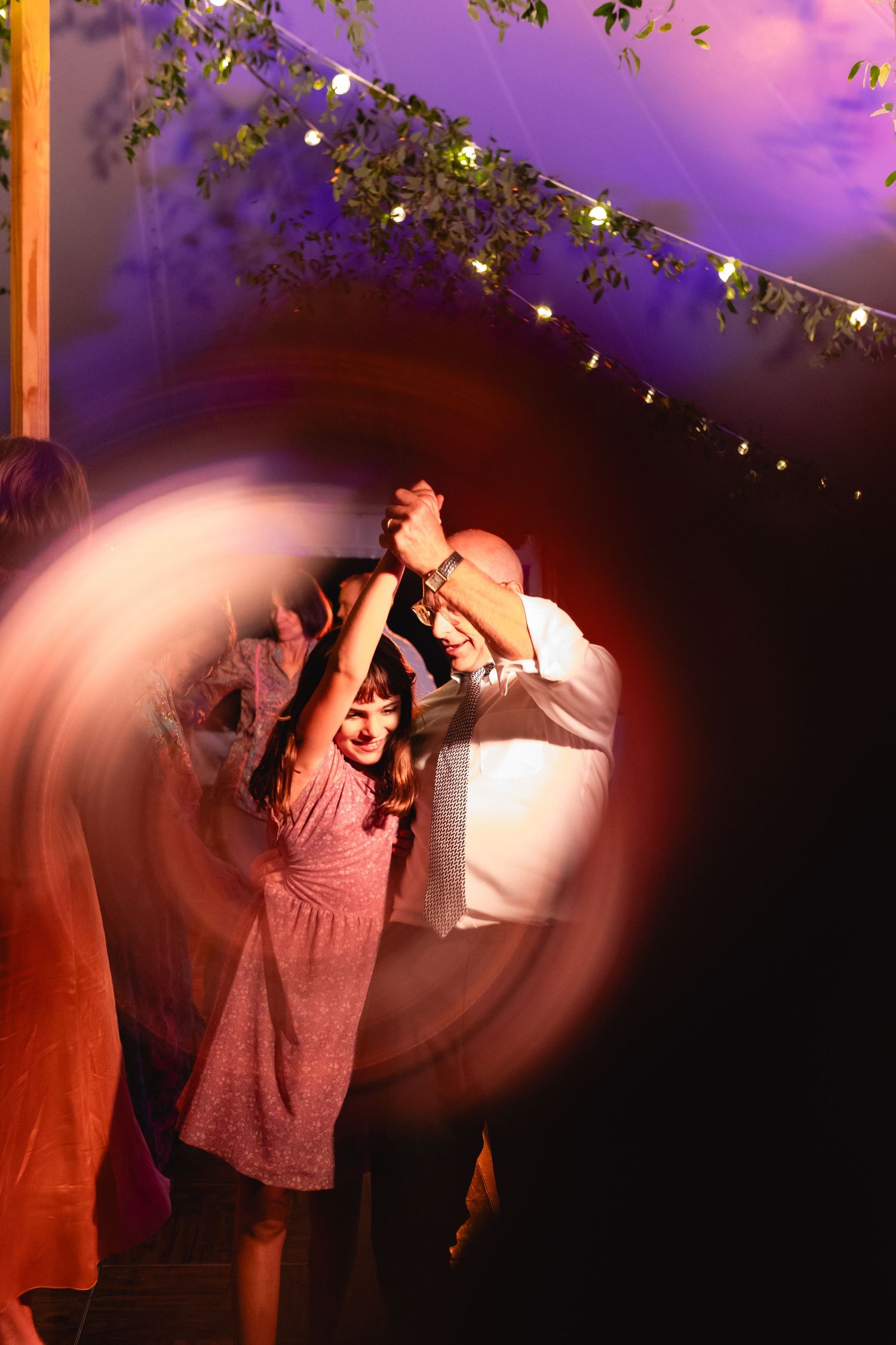 Guests dance under string lights at an outdoor wedding reception at night.
