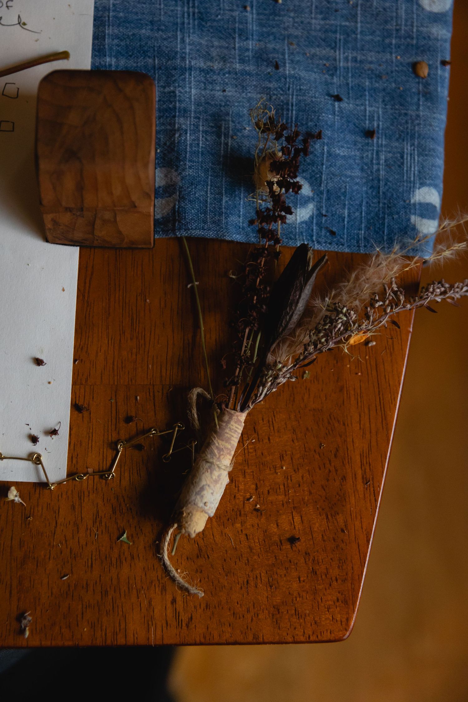 Dried flowers tied with twine rest on a rustic wooden surface against a blue fabric background.