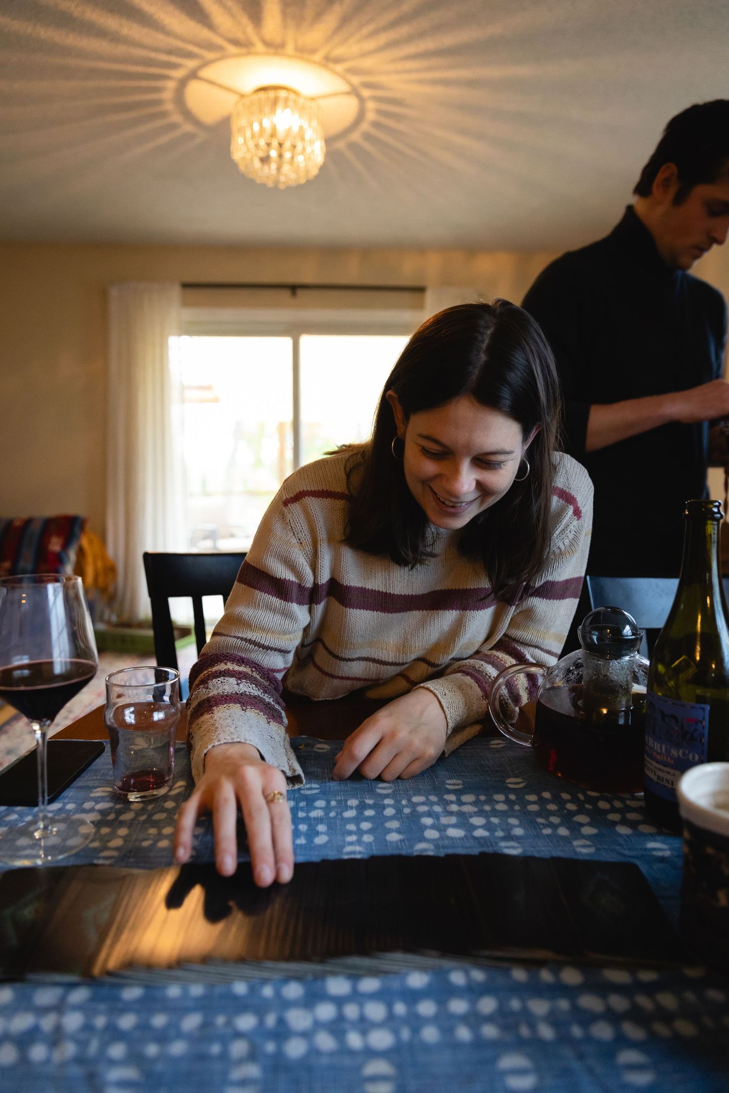 Person in striped sweater looks down at table under elegant chandelier lighting at gathering.