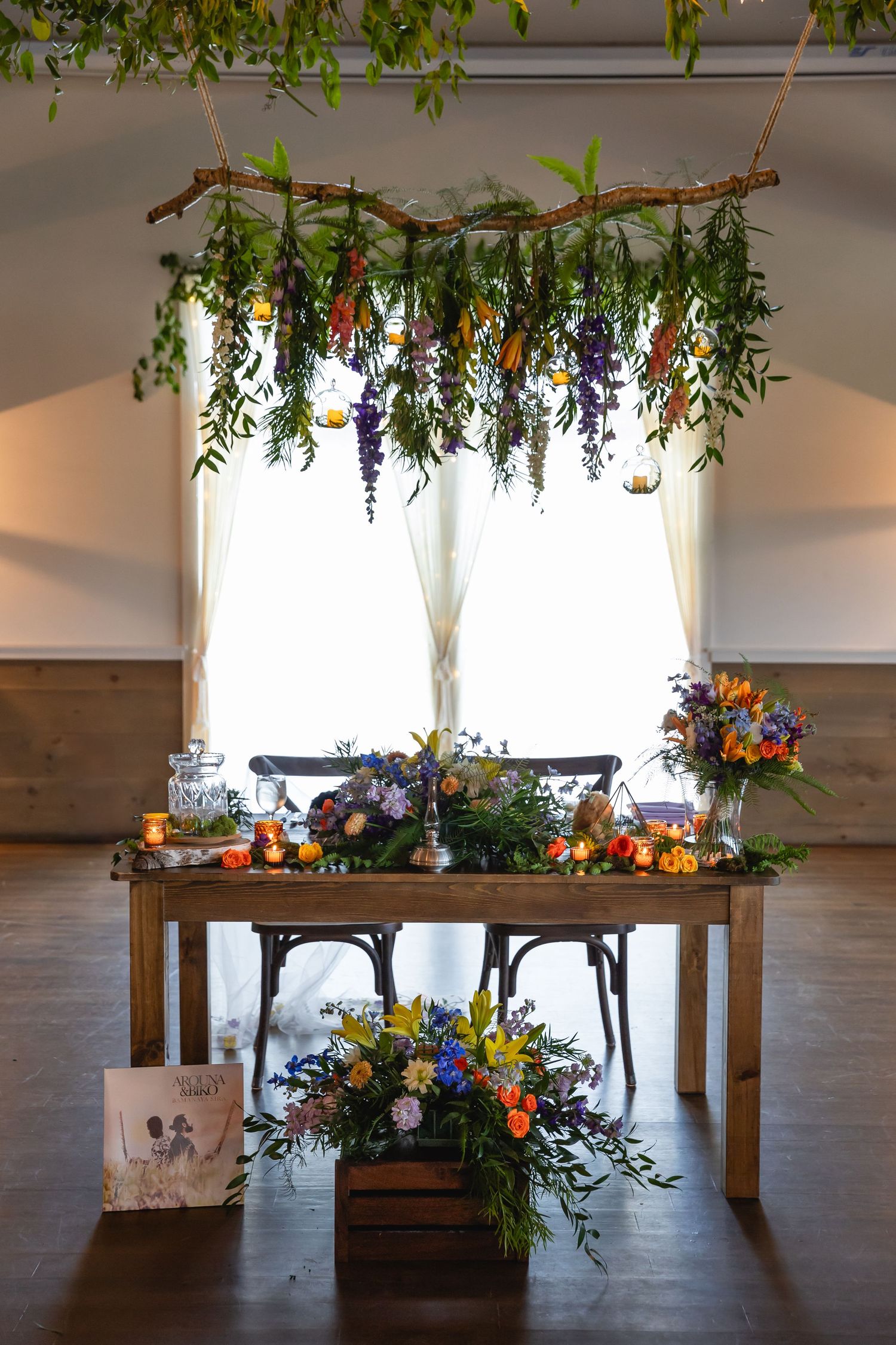 Elegant sweetheart table with suspended floral installation and colorful flower arrangements.
