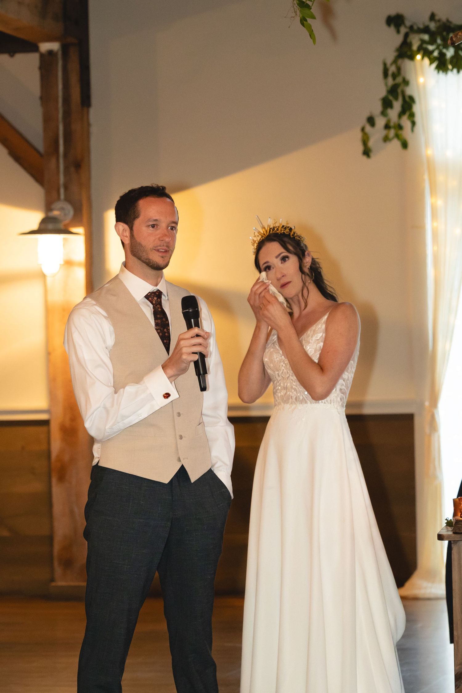 Couple giving speeches during wedding reception with decorative floral backdrop.