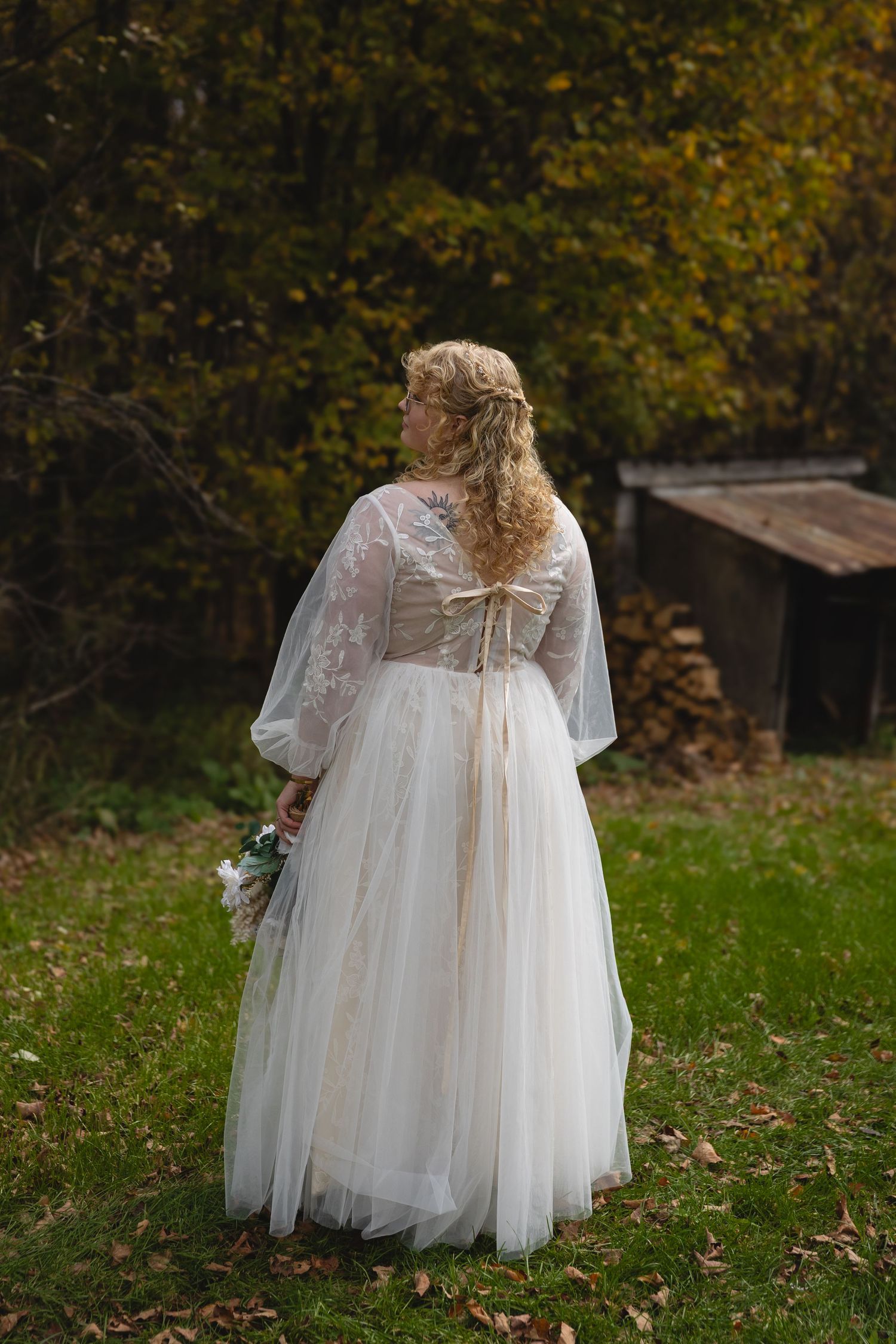 Back view of a wedding dress with sheer lace sleeves and tulle skirt in an autumn setting.