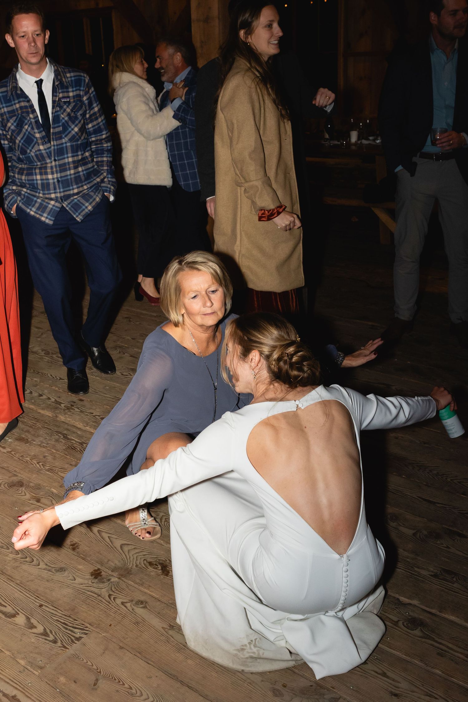 Two people dancing casually on a wooden floor at a social gathering with others visible in the background.