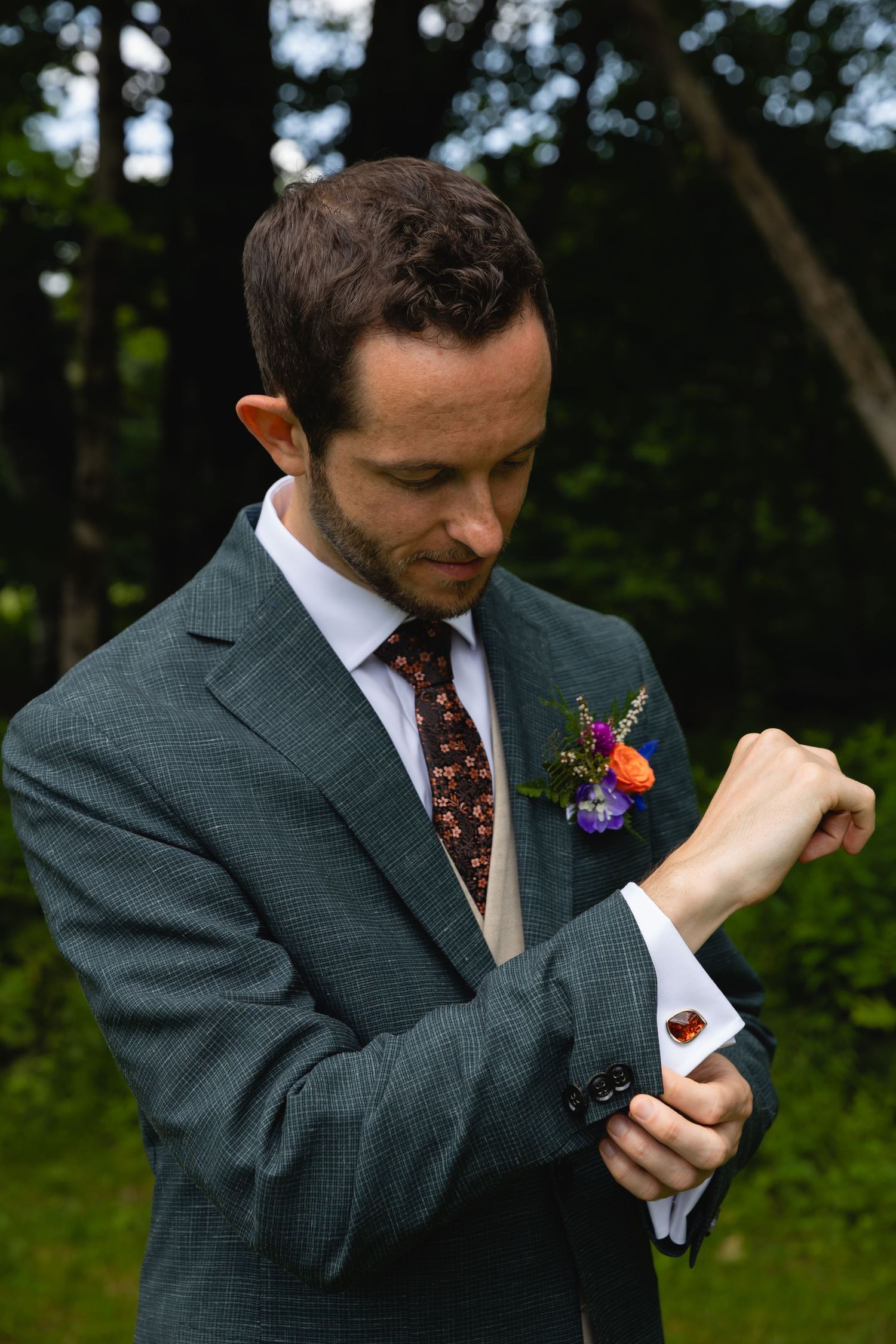 Close-up of groom adjusting cufflink while wearing gray suit with floral boutonniere.